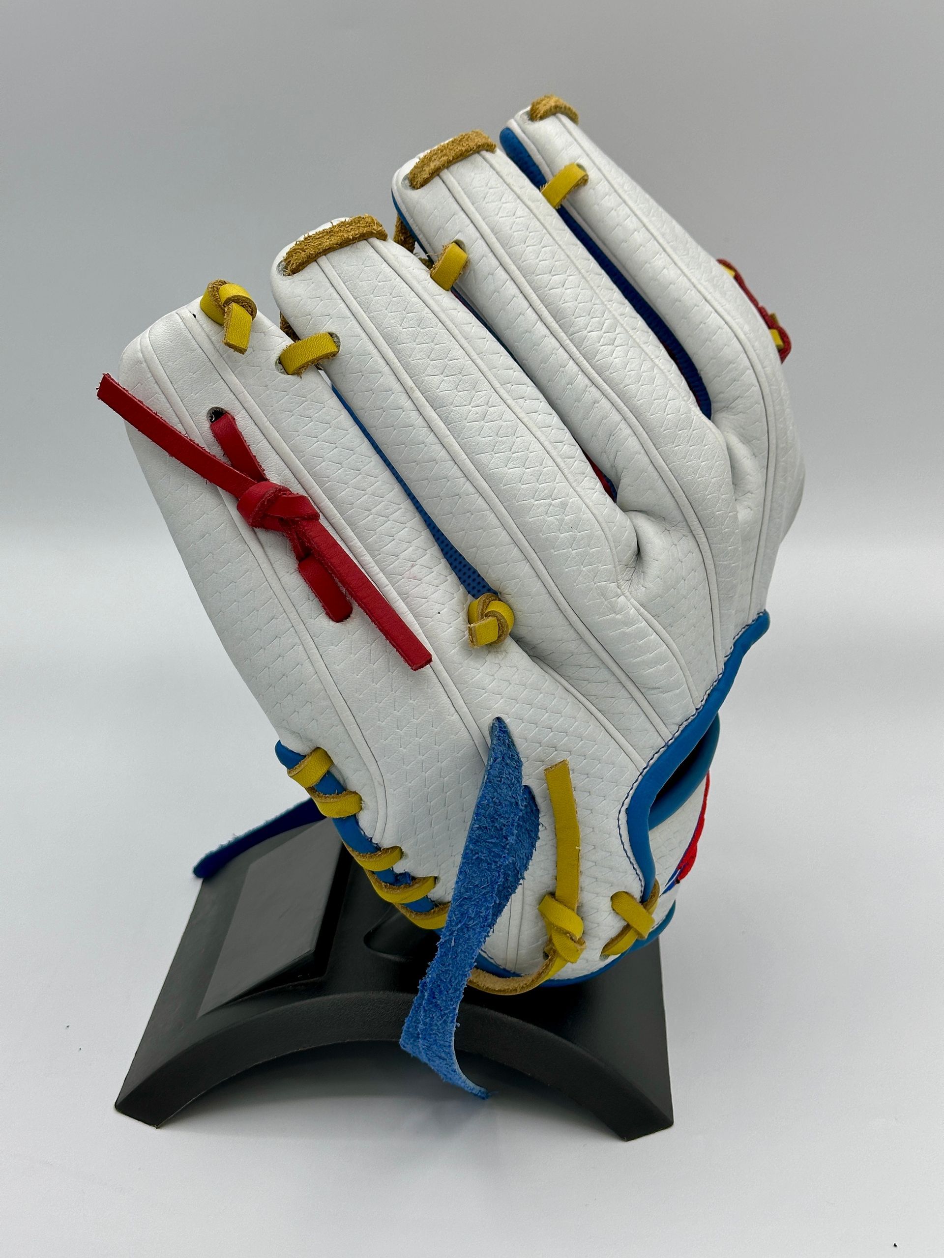 A white baseball glove with red yellow and blue stitching