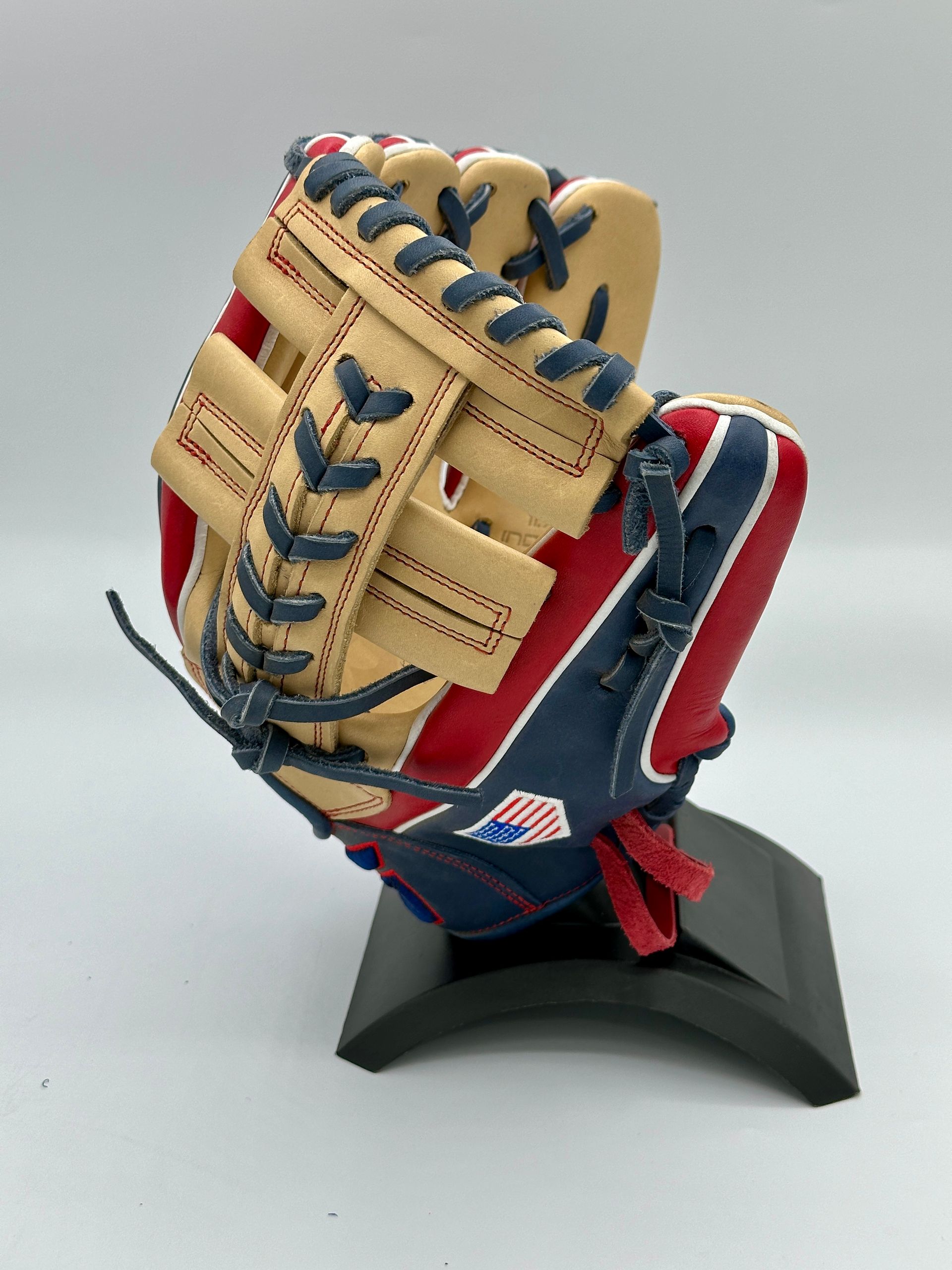 A red , white and blue baseball glove is sitting on a black stand.