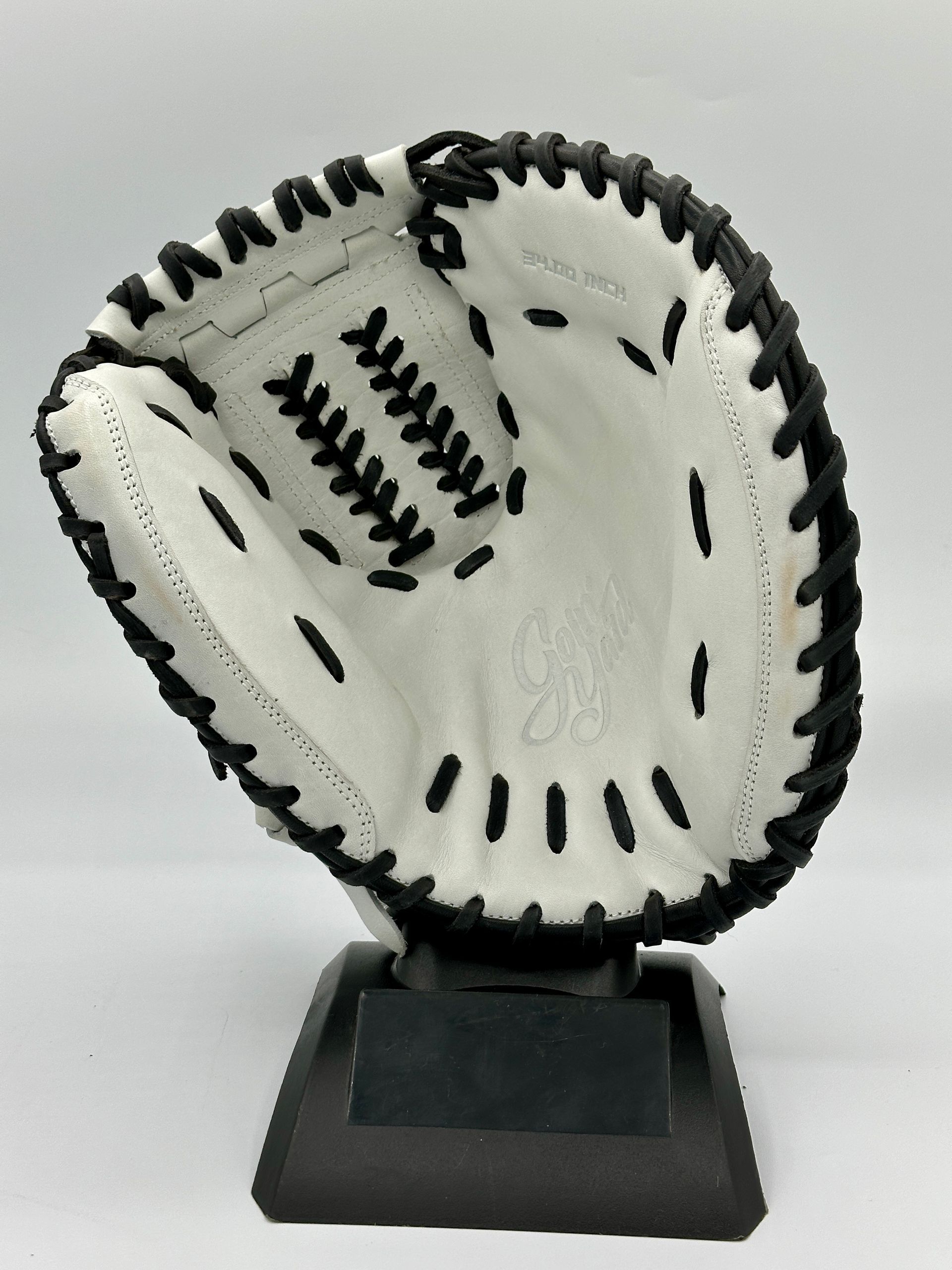 A white baseball glove with black stitching is on a black base