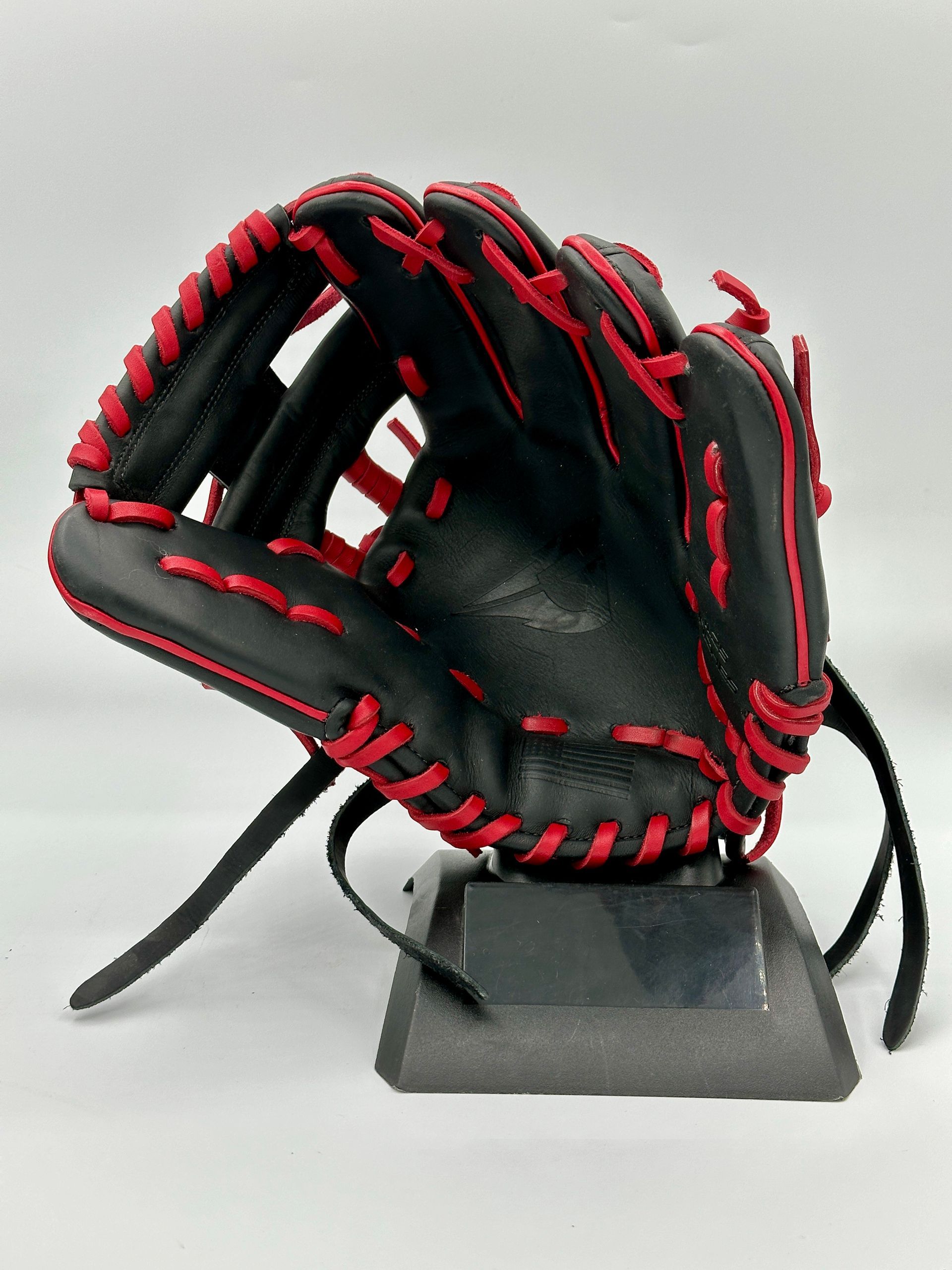 A black baseball glove with red stitching is on a stand