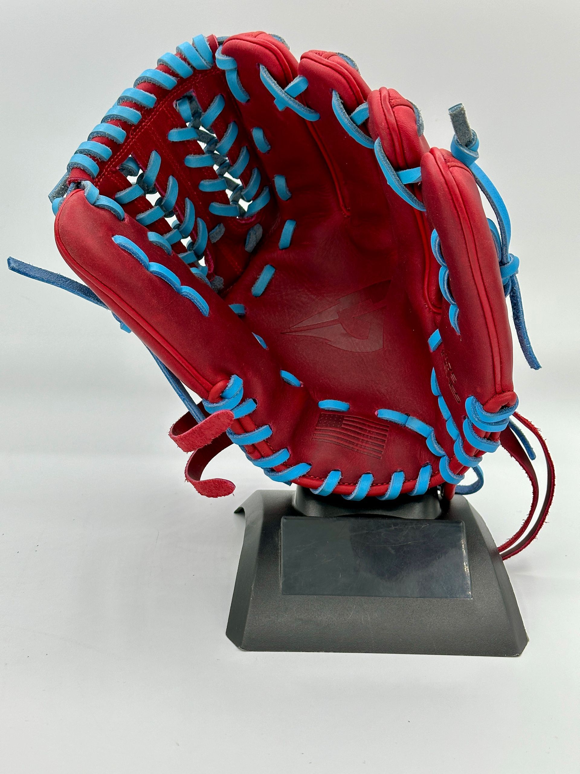A red baseball glove with blue stitching is on a stand