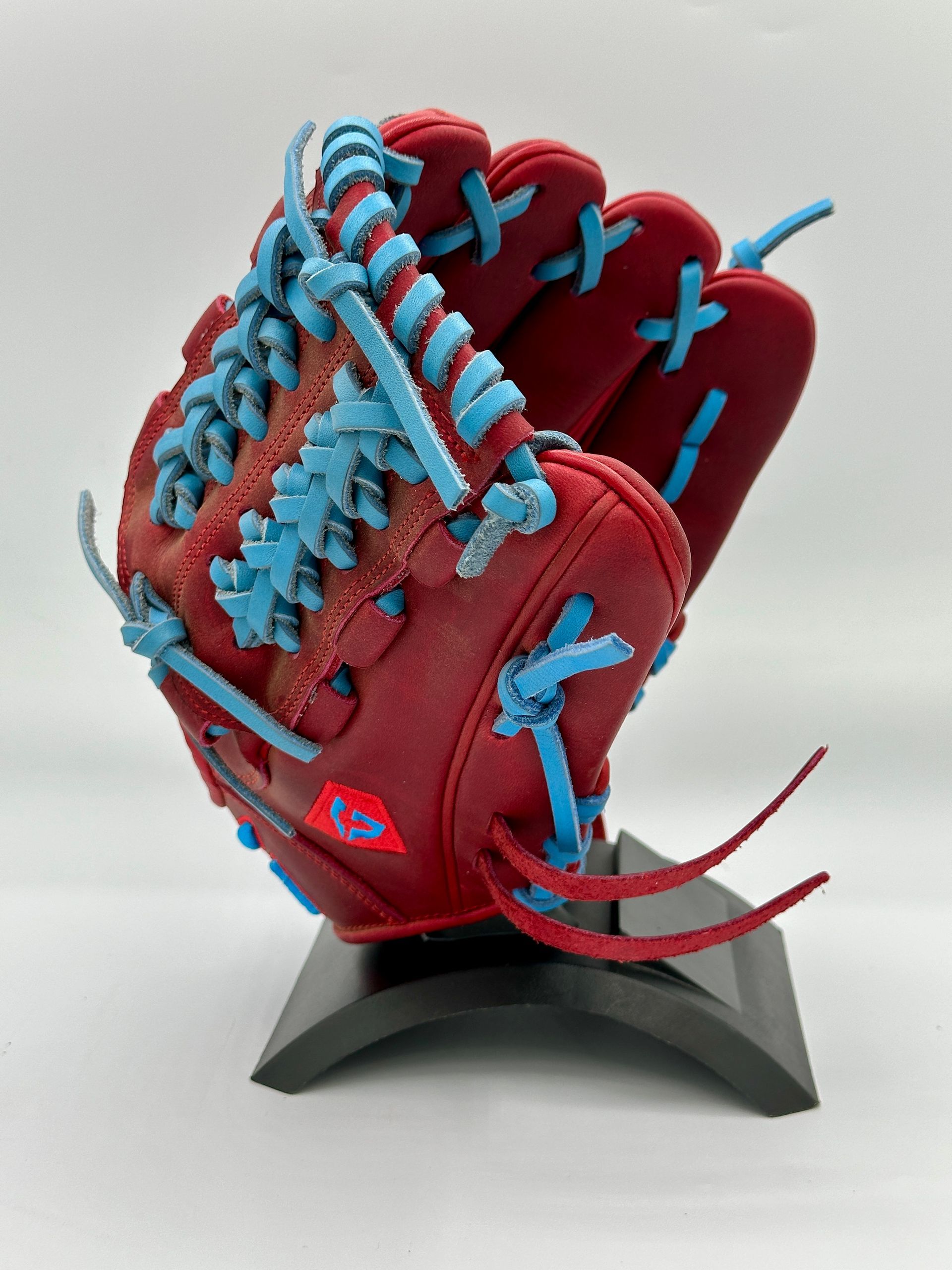 A red baseball glove with blue laces is on a stand