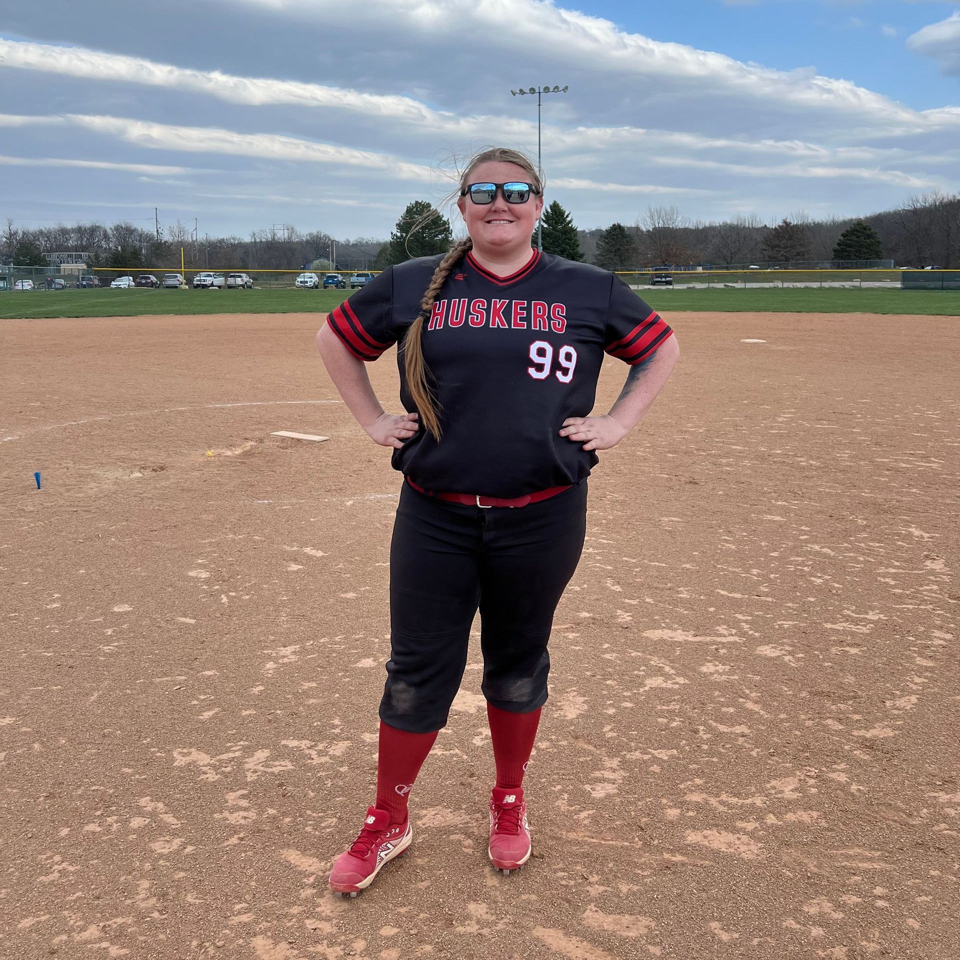 Softball player in black and red uniform, hands on hips, on a dirt field.