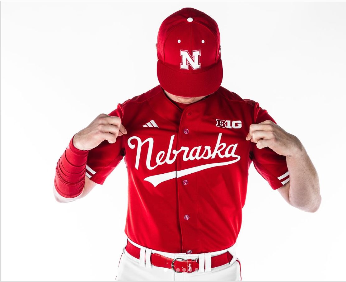 Nebraska baseball player in red uniform and hat, displaying jersey, white pants, and red wristband.