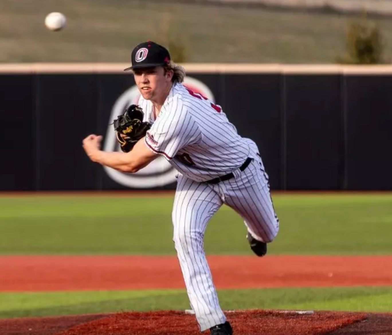 Baseball pitcher in striped uniform throws a ball on a baseball field.