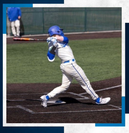 Baseball player in blue and white uniform swings bat at a ball on a field.