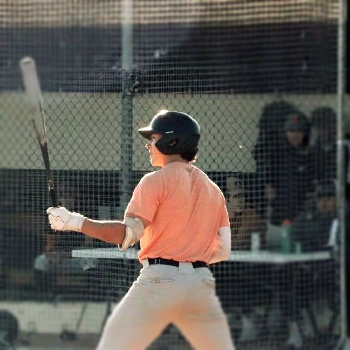 Baseball player in orange shirt and helmet at bat, ready to swing.