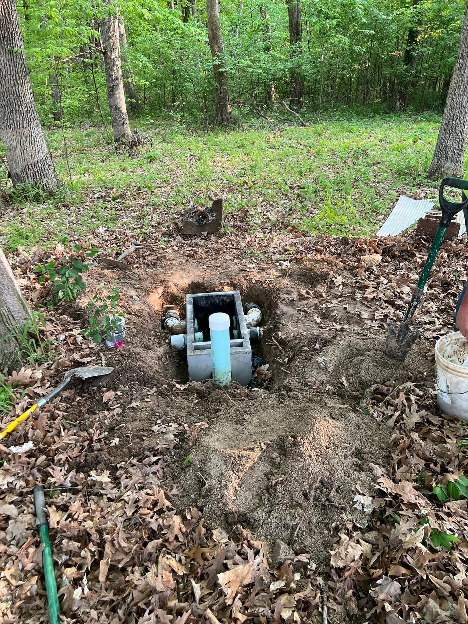 Trench with exposed blue pipe fittings in a wooded area, surrounded by dirt and leaves