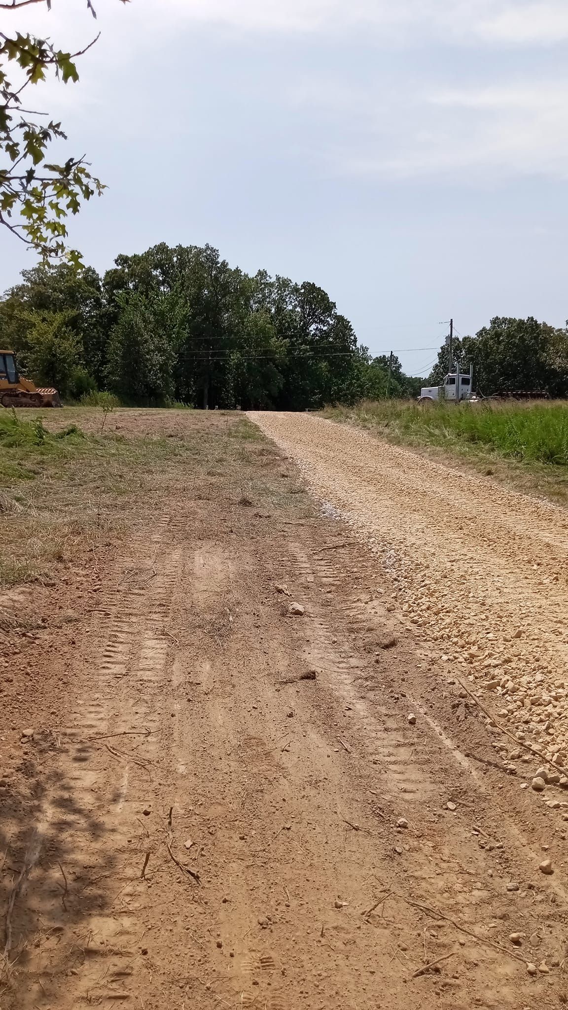 Dirt path cutting through a dry field toward trees under a partly cloudy sky