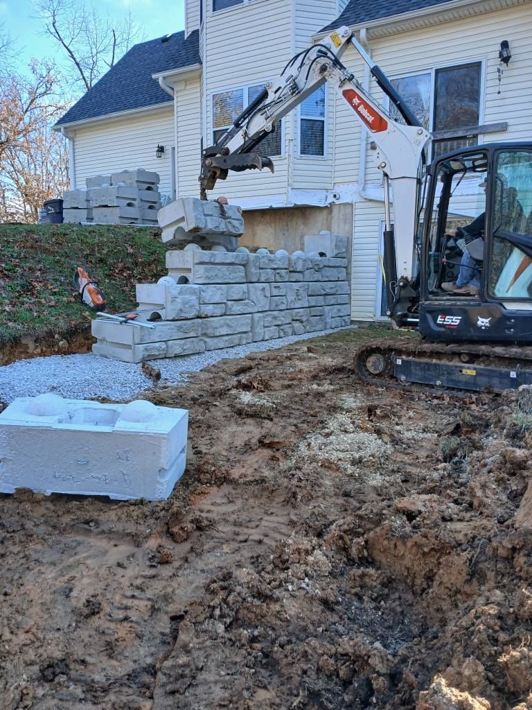Excavator lifting concrete blocks beside a house during demolition or landscaping work
