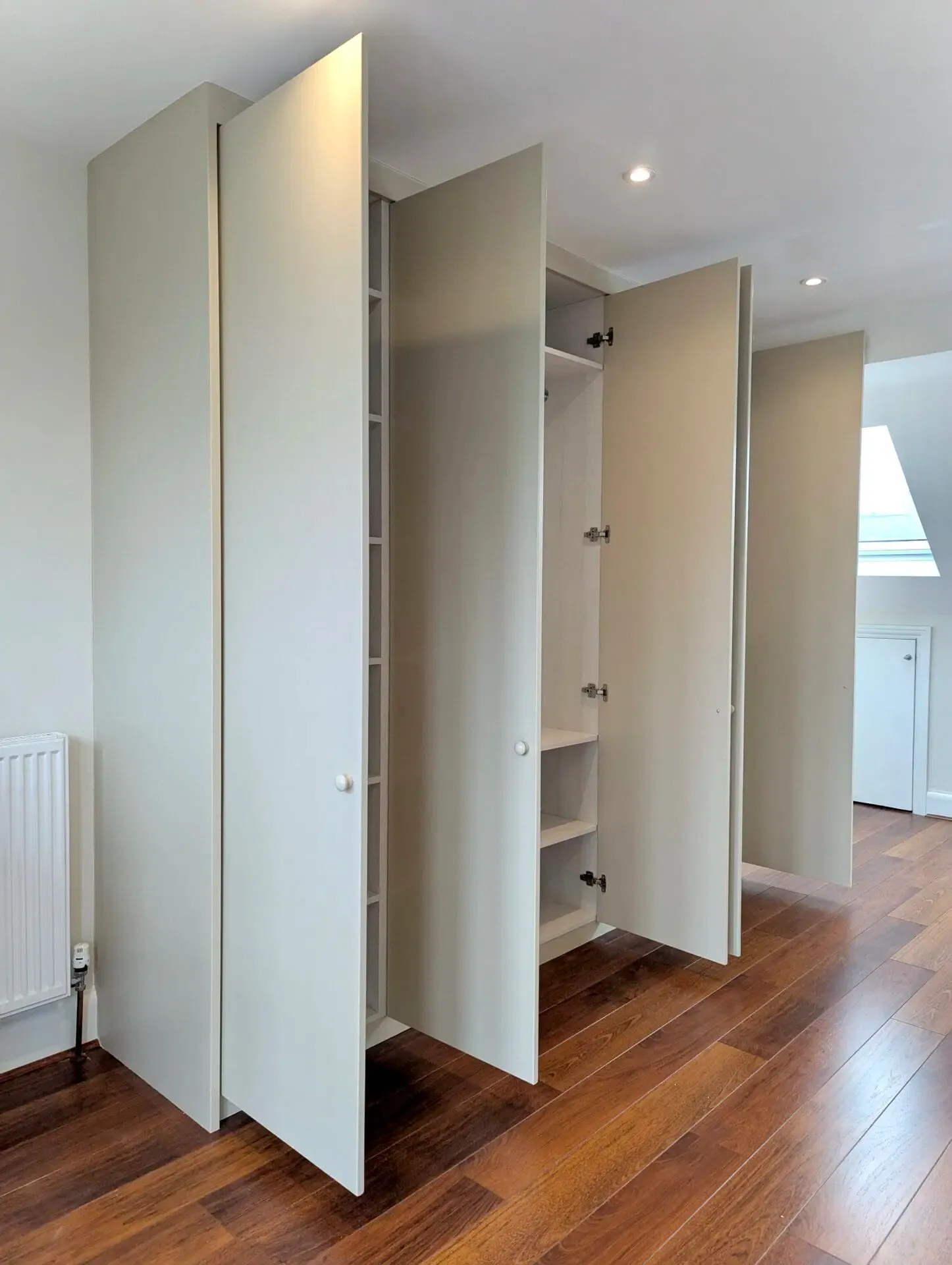 Built-in closet with four light-colored doors open on a hardwood floor.