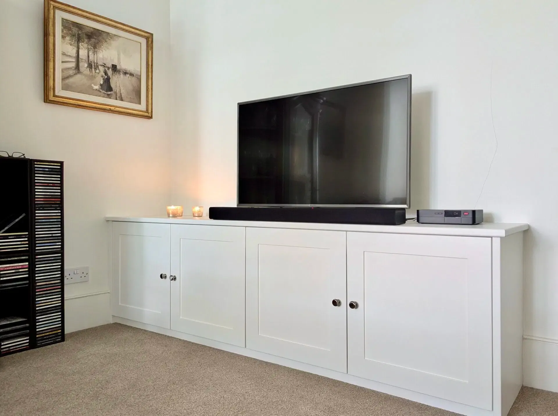White cabinet with TV and soundbar against a white wall; framed picture above.