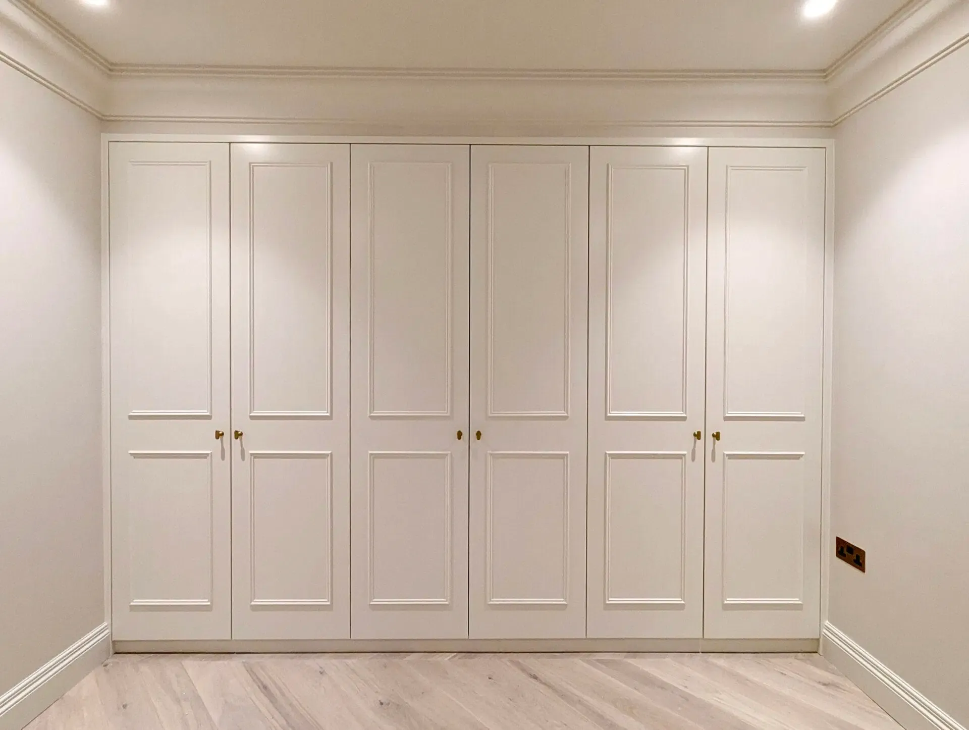 White built-in wardrobe with six paneled doors against white walls and light wood floor.