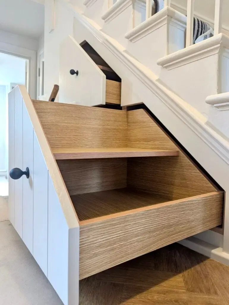 White cabinet with a pull-out drawer built into the staircase, offering storage.