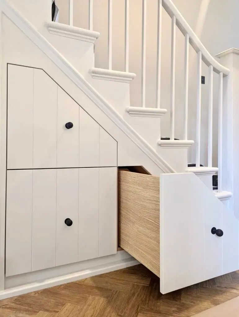 White under-stair storage drawers, one open, with a wooden interior, in a home.