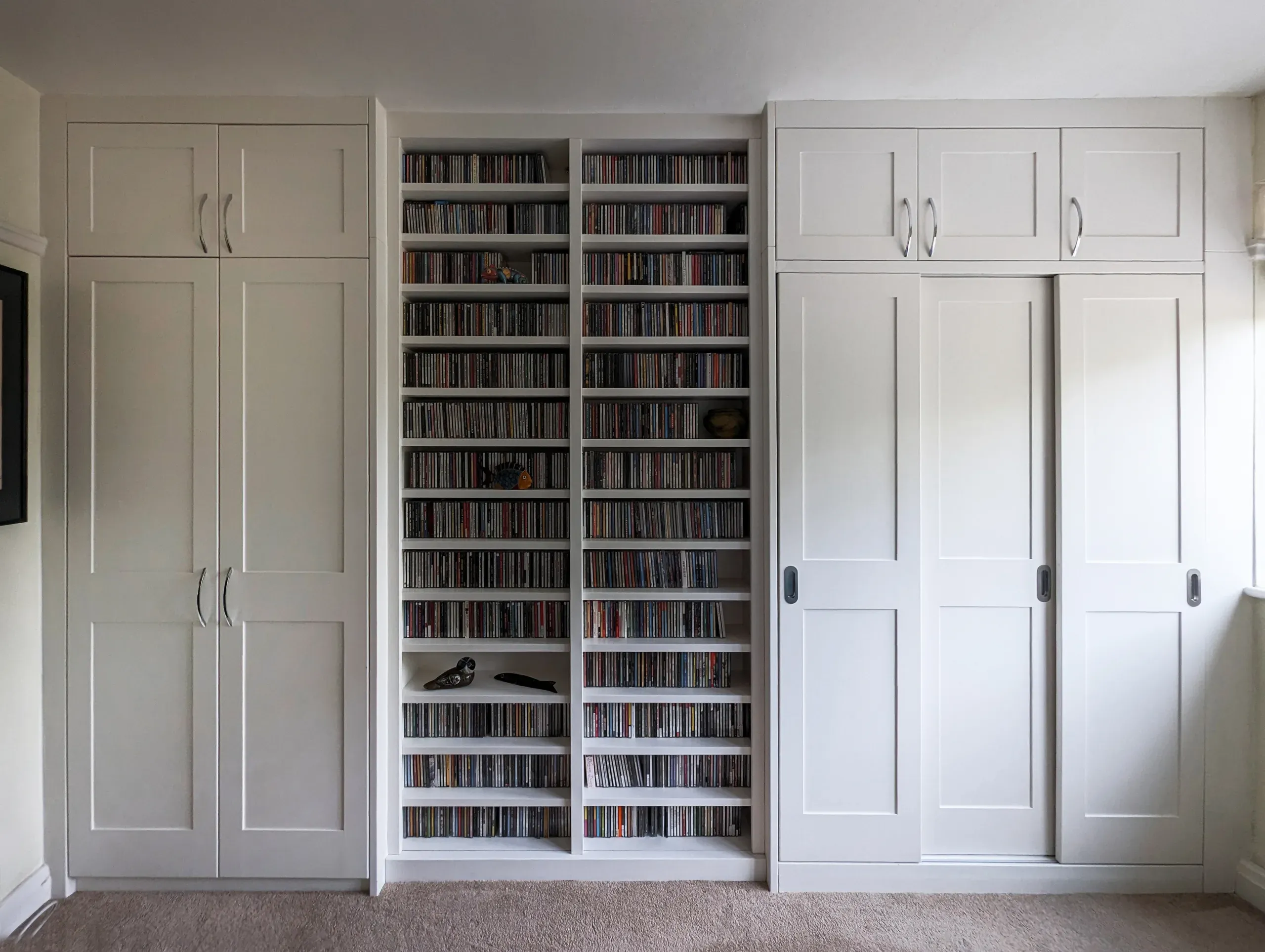 Built-in white shelves and cabinets filled with CDs and other items in a room with carpet.