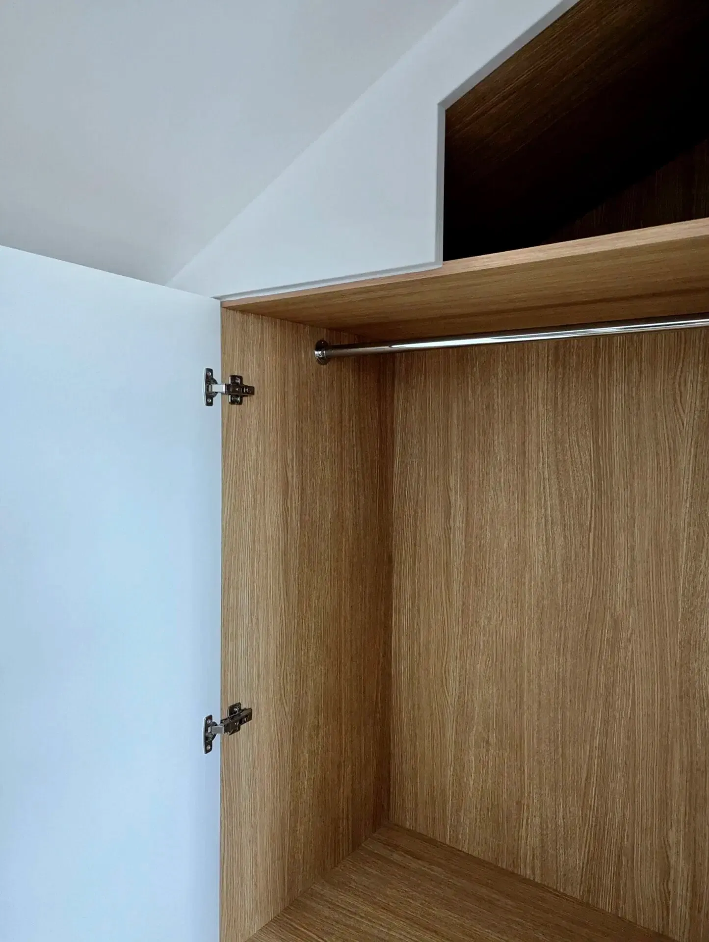 Interior view of an open wardrobe with a hanging rod. Wooden panels with a white door.