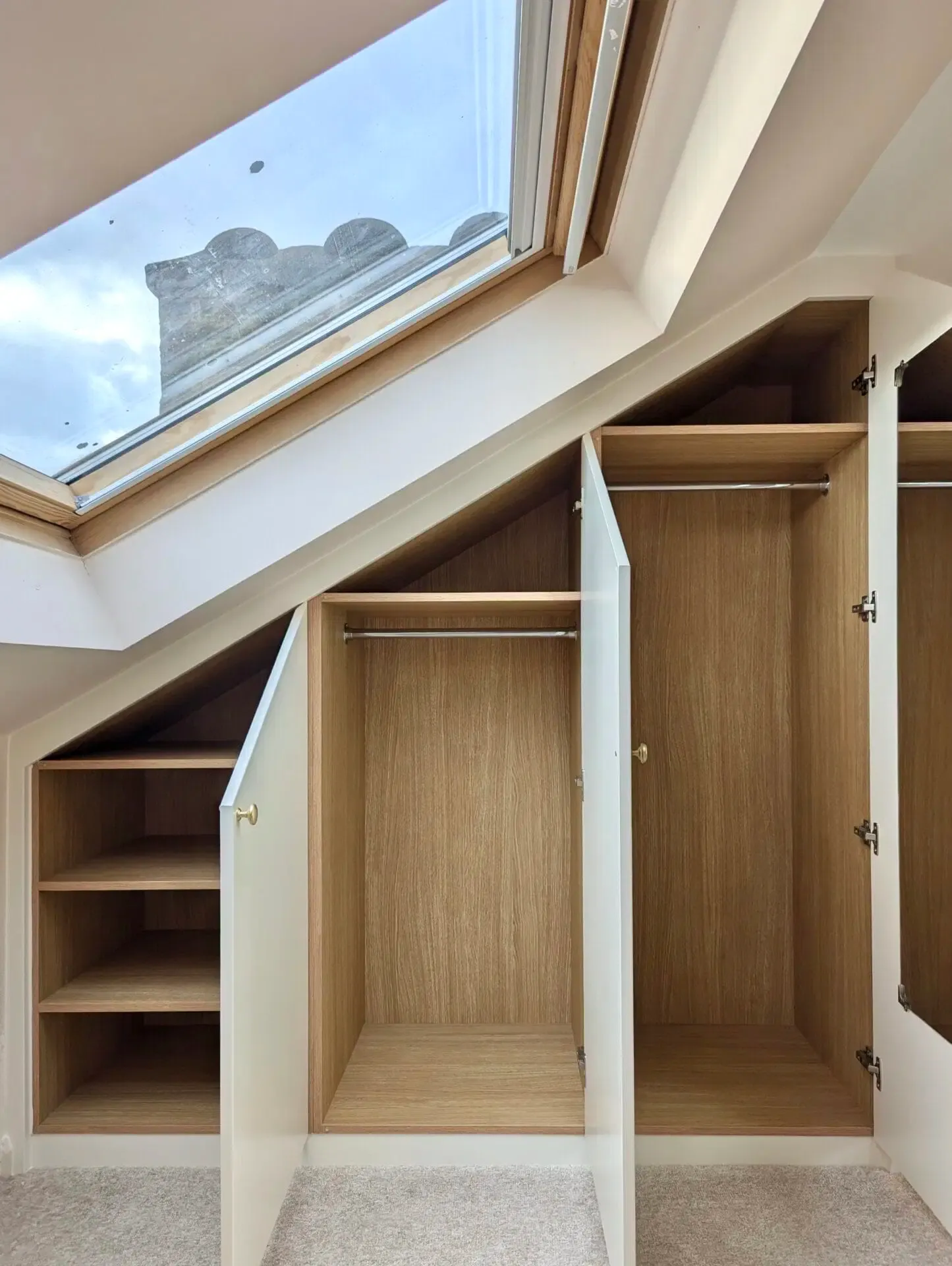 Custom closet built into angled ceiling; wood shelves and hanging space. White doors, natural wood interior.