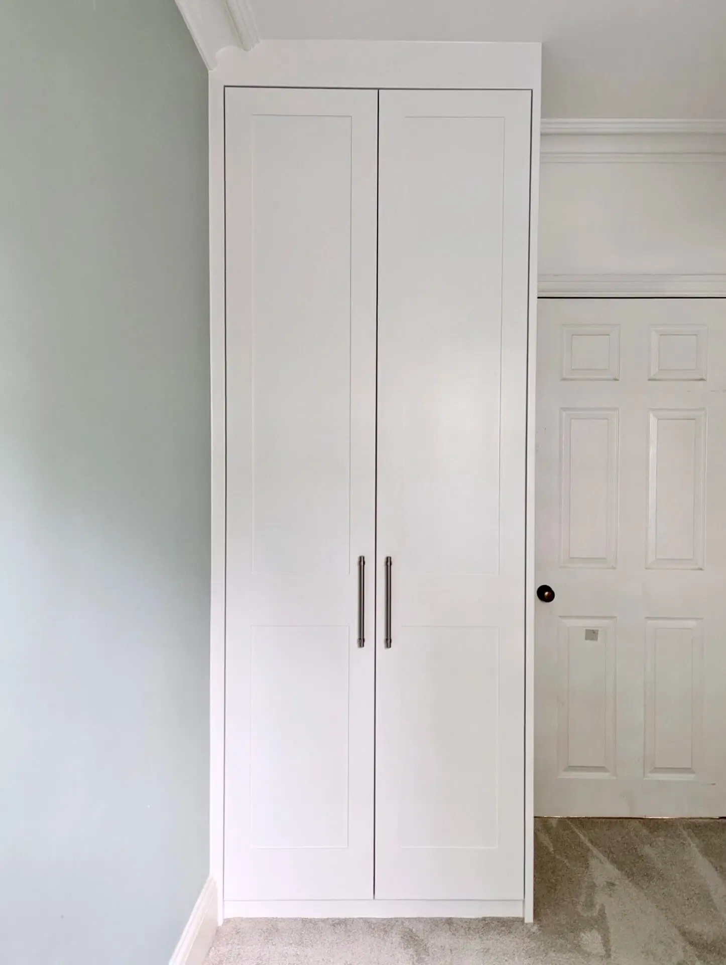 White closet with two doors and silver handles next to a pale blue wall and a white door.