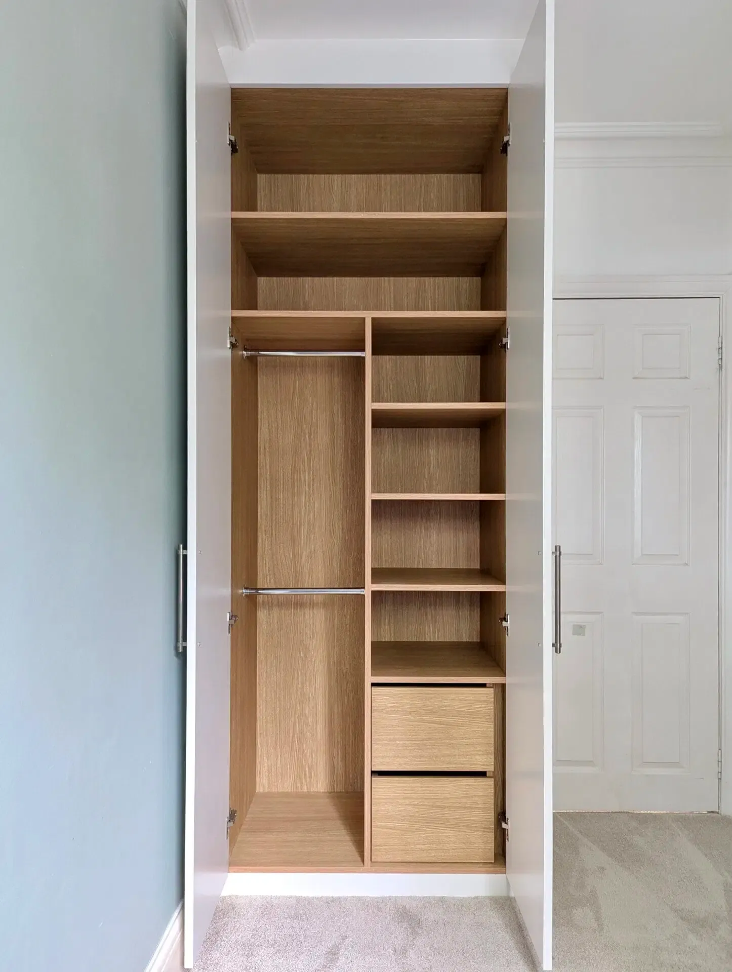 Open white wardrobe with wooden shelves, drawers, and hanging rod. Interior view.