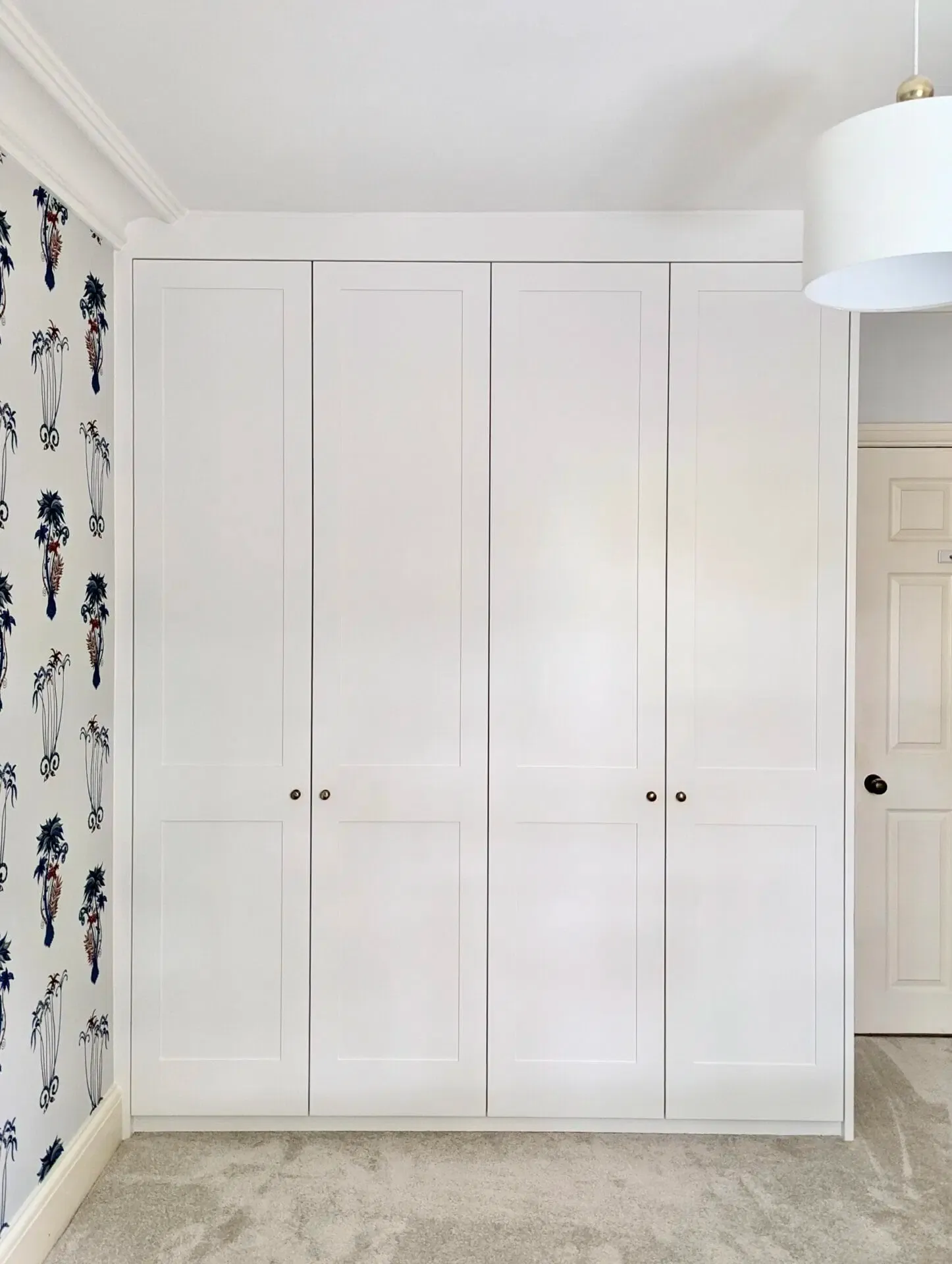 White four-door wardrobe against a patterned wallpapered wall.