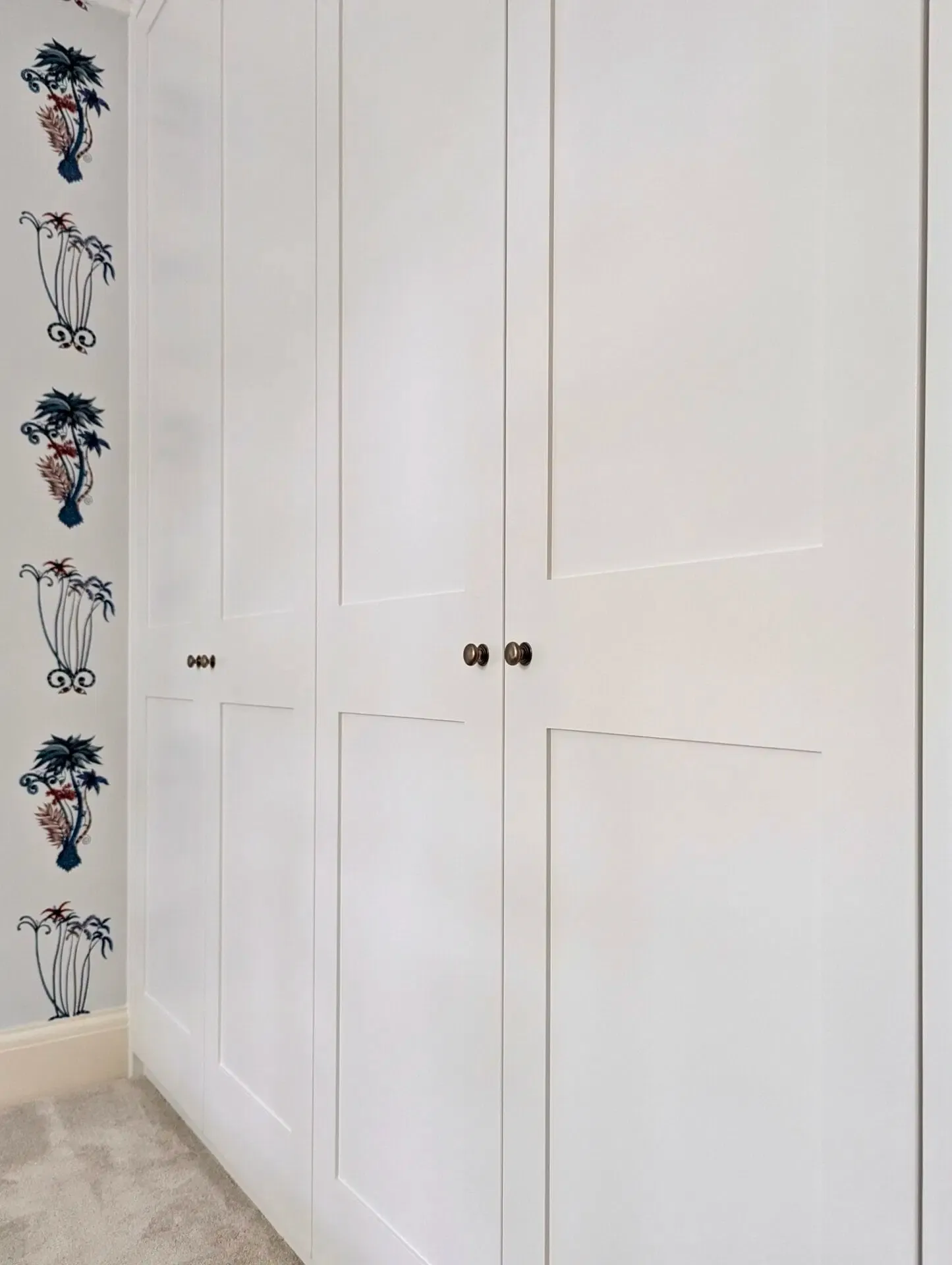 White closet with dark knobs and floral wallpaper.