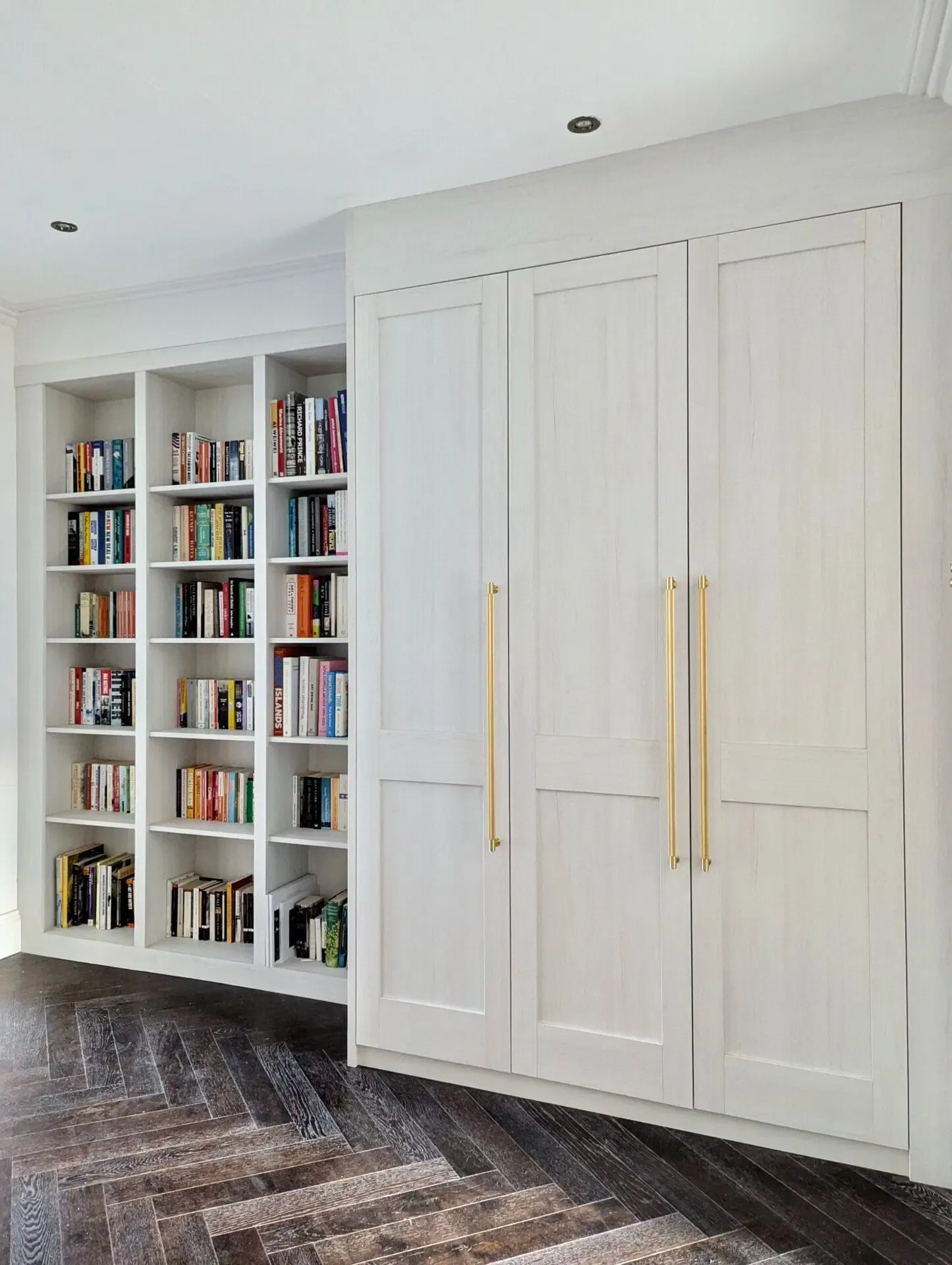 Built-in white bookshelves and closet with gold handles. Dark wood floor, bright room.