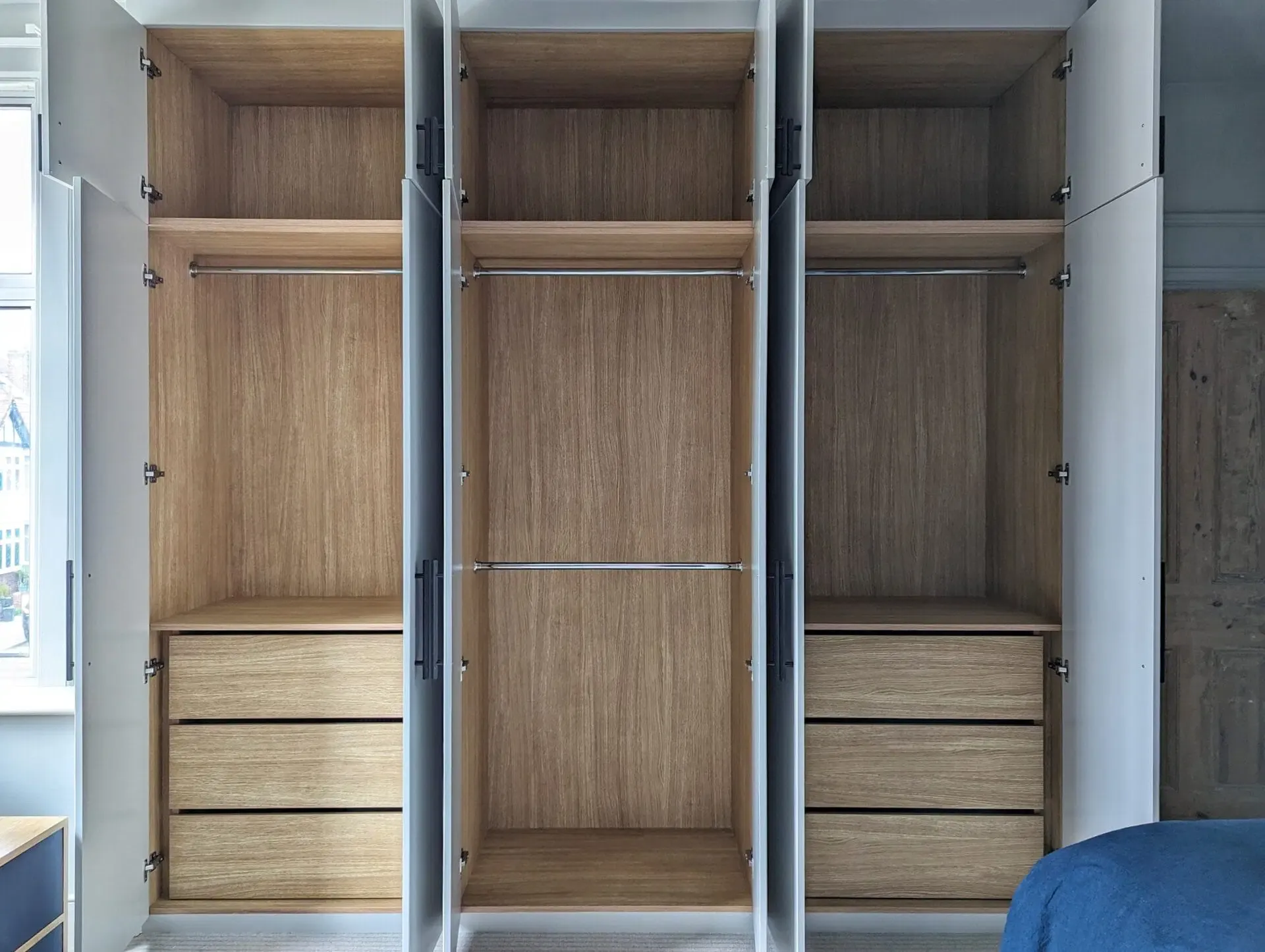 Open, empty wooden closet with three sections and drawers.