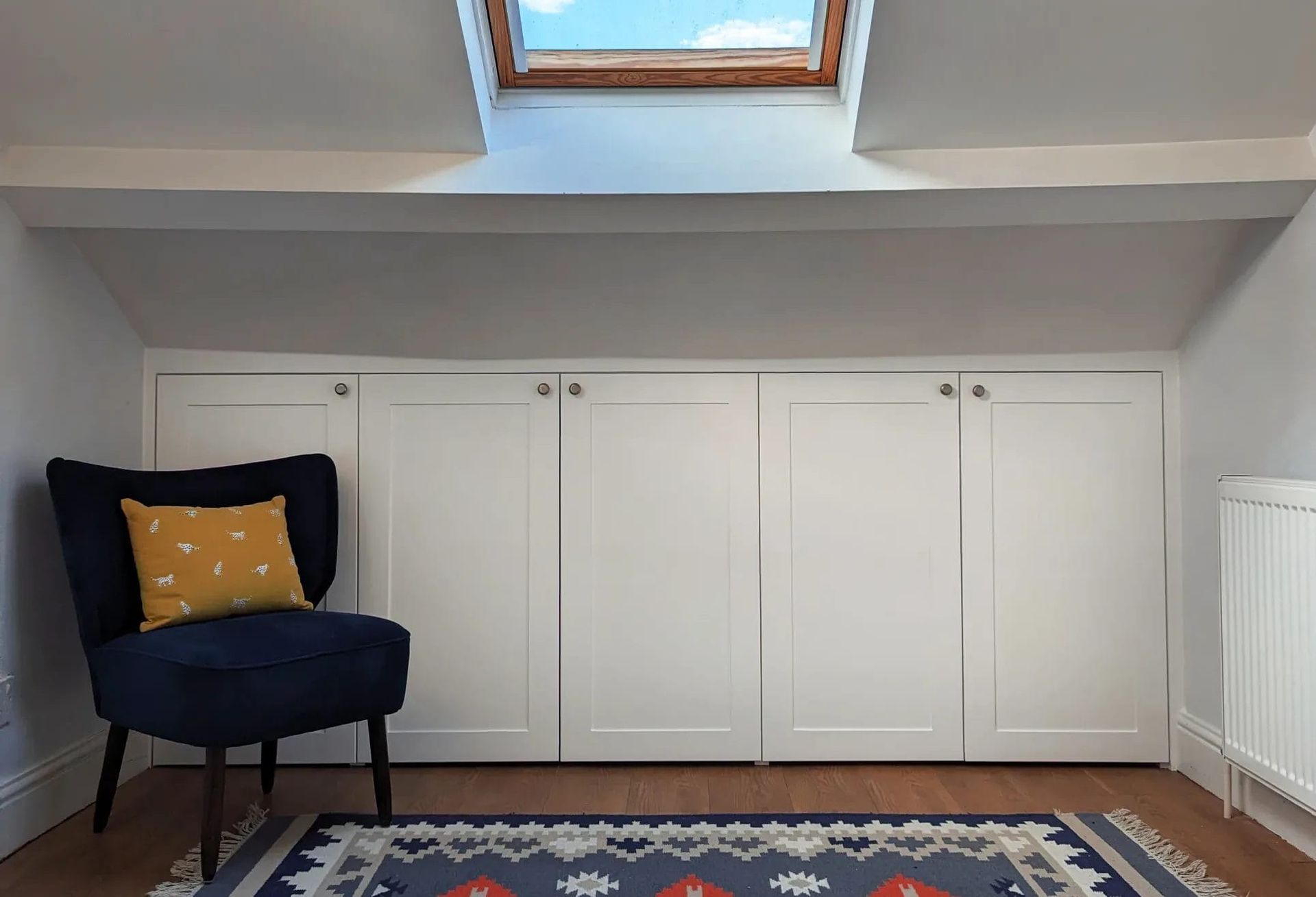 Room with white storage cabinets, blue chair, rug, and skylight.