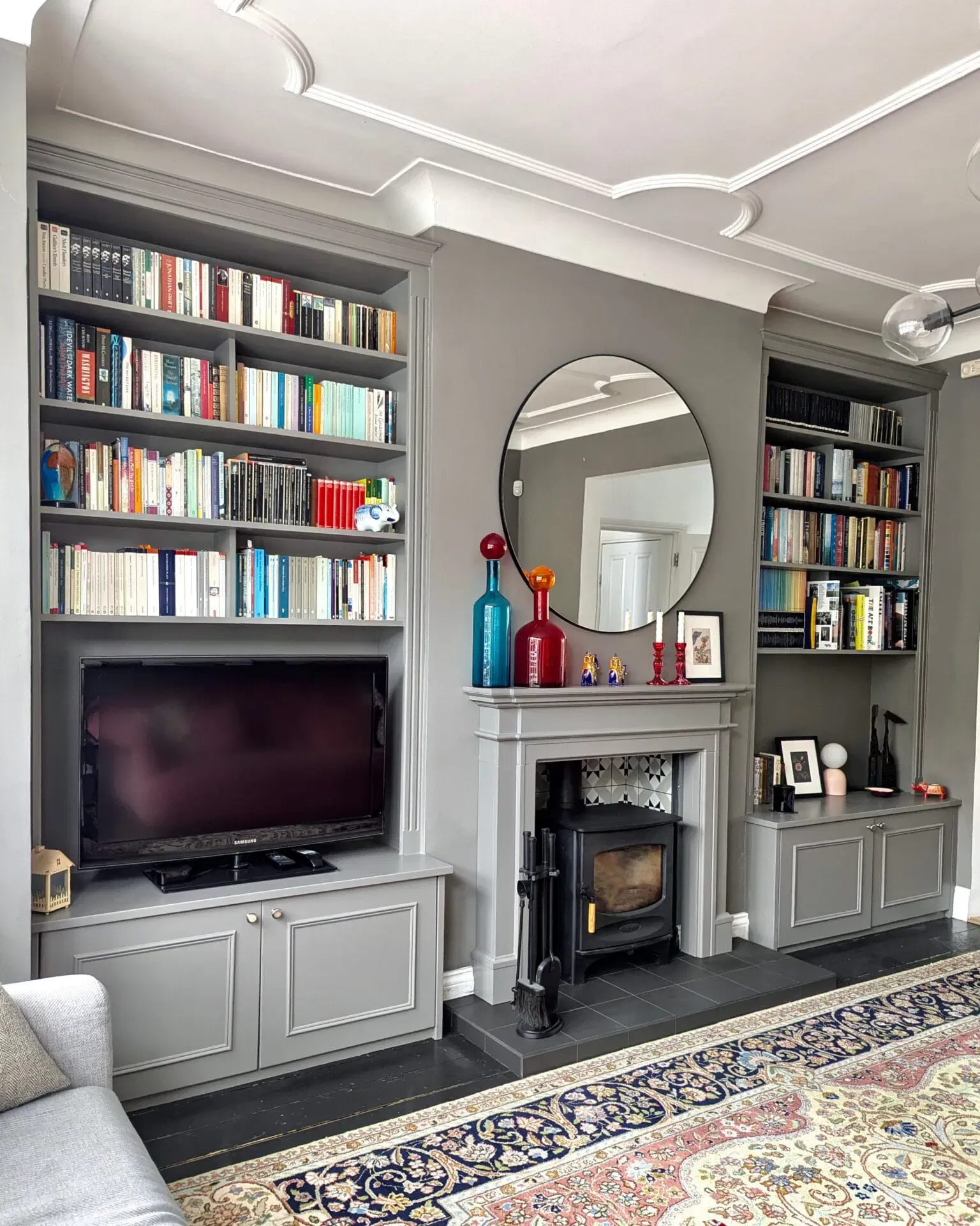 Living room with gray built-in bookshelves, a fireplace, and a round mirror. Books and decor are visible.