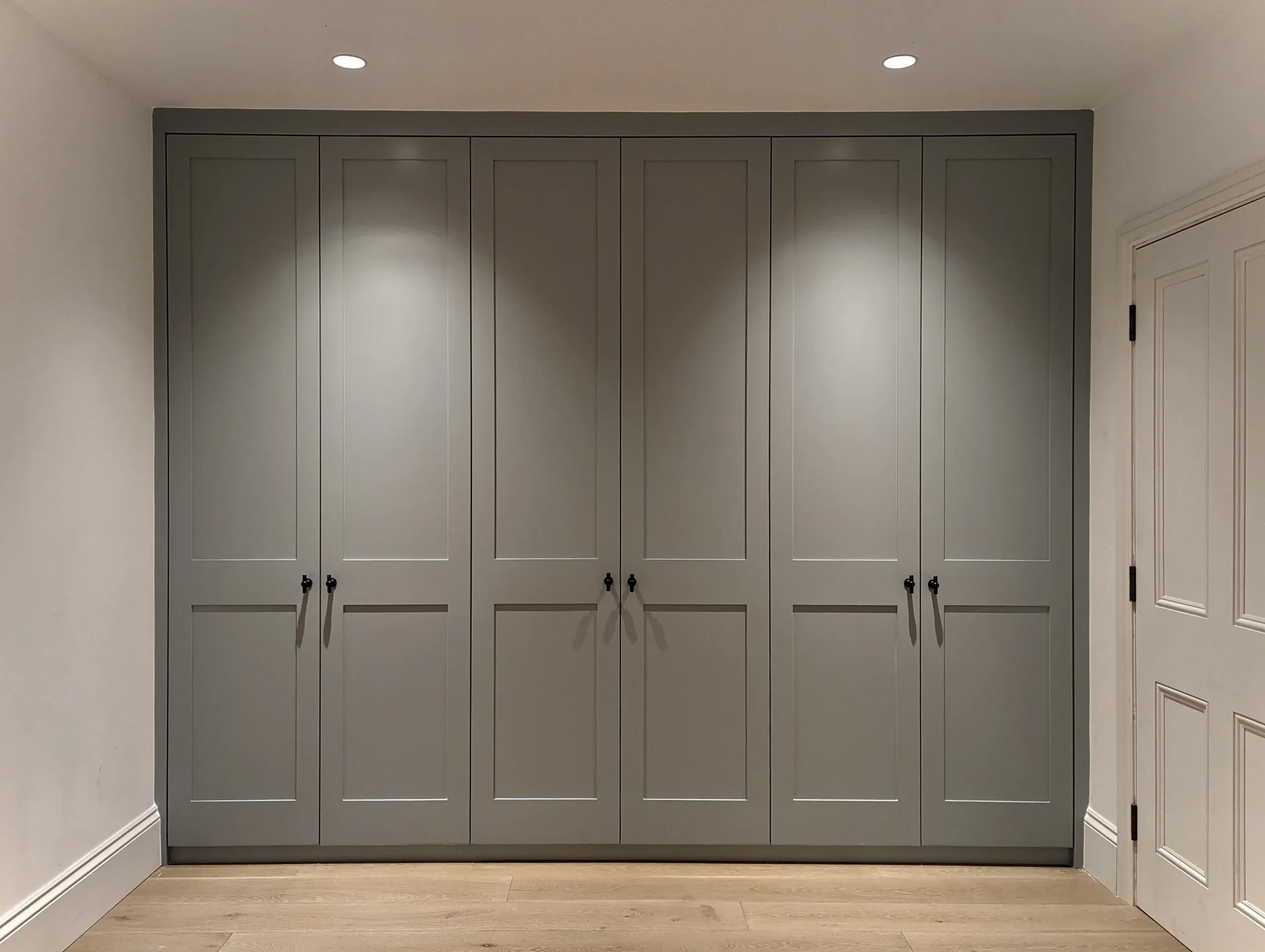 Gray built-in closet with six doors and black handles, under recessed lighting.
