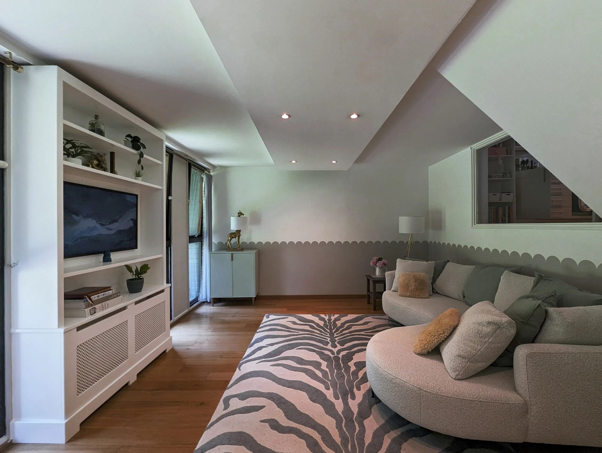 Living room with a curved sofa, patterned rug, TV, and built-in shelving.