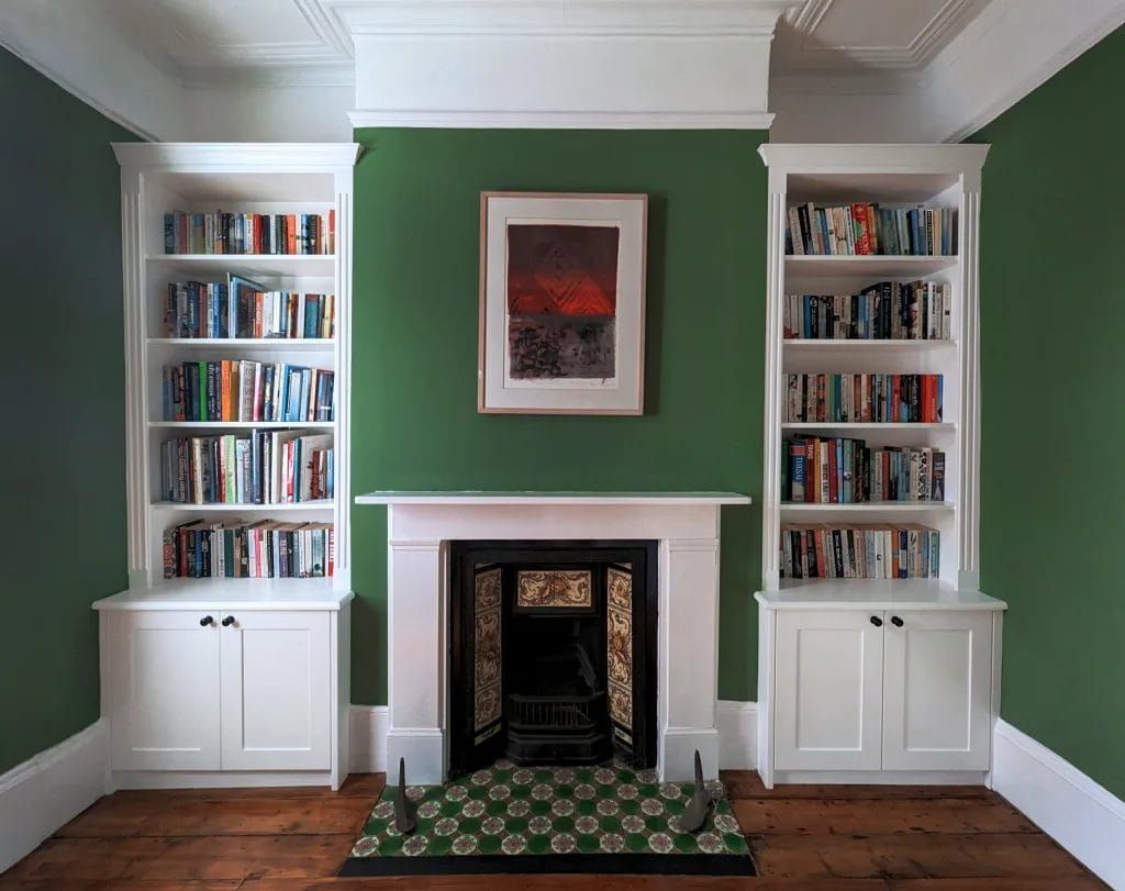 White bookshelves flank a fireplace, green wall, and framed artwork.