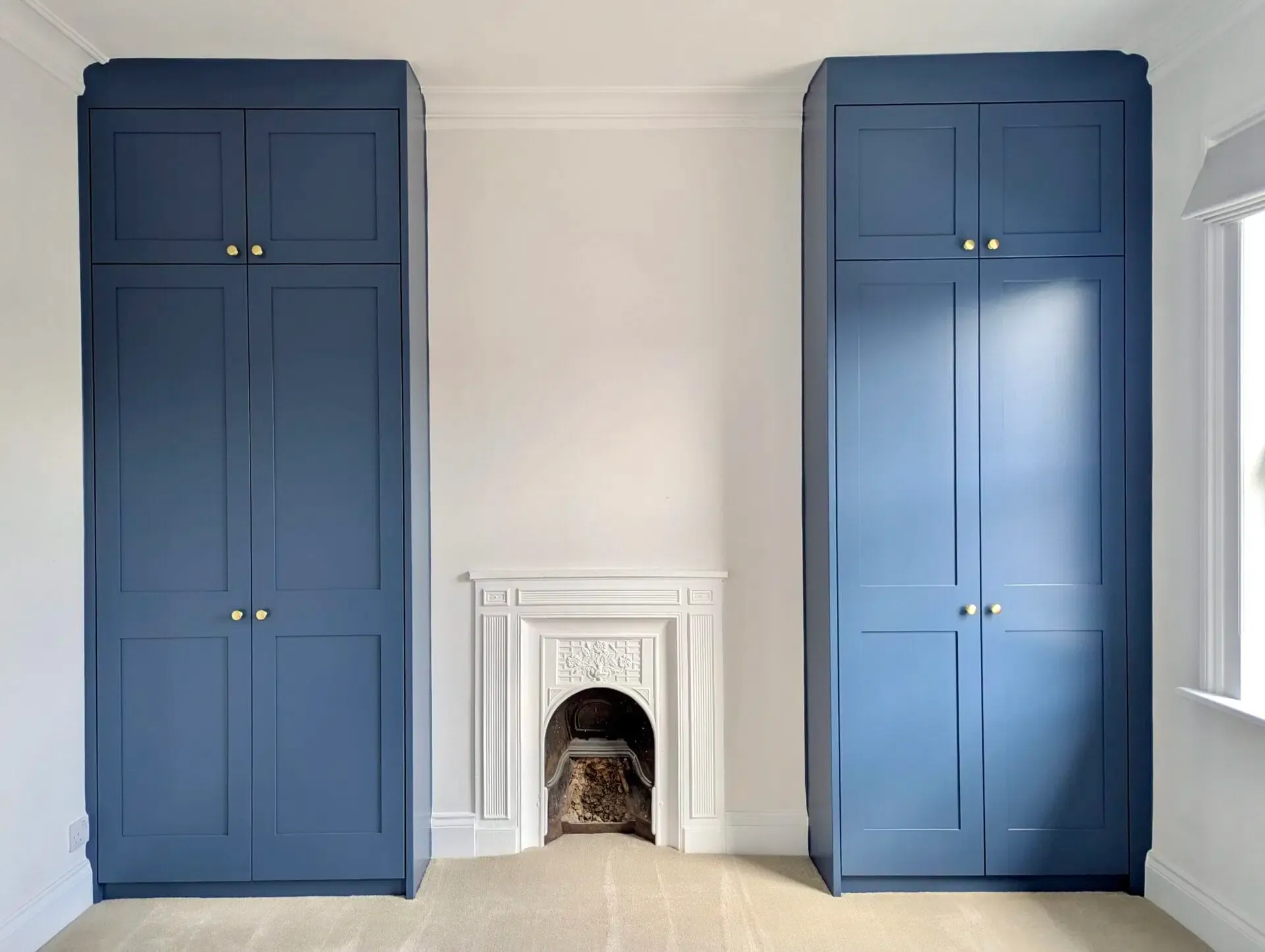 Two tall blue wardrobes flanking a white fireplace in a room with light-colored walls and carpet.
