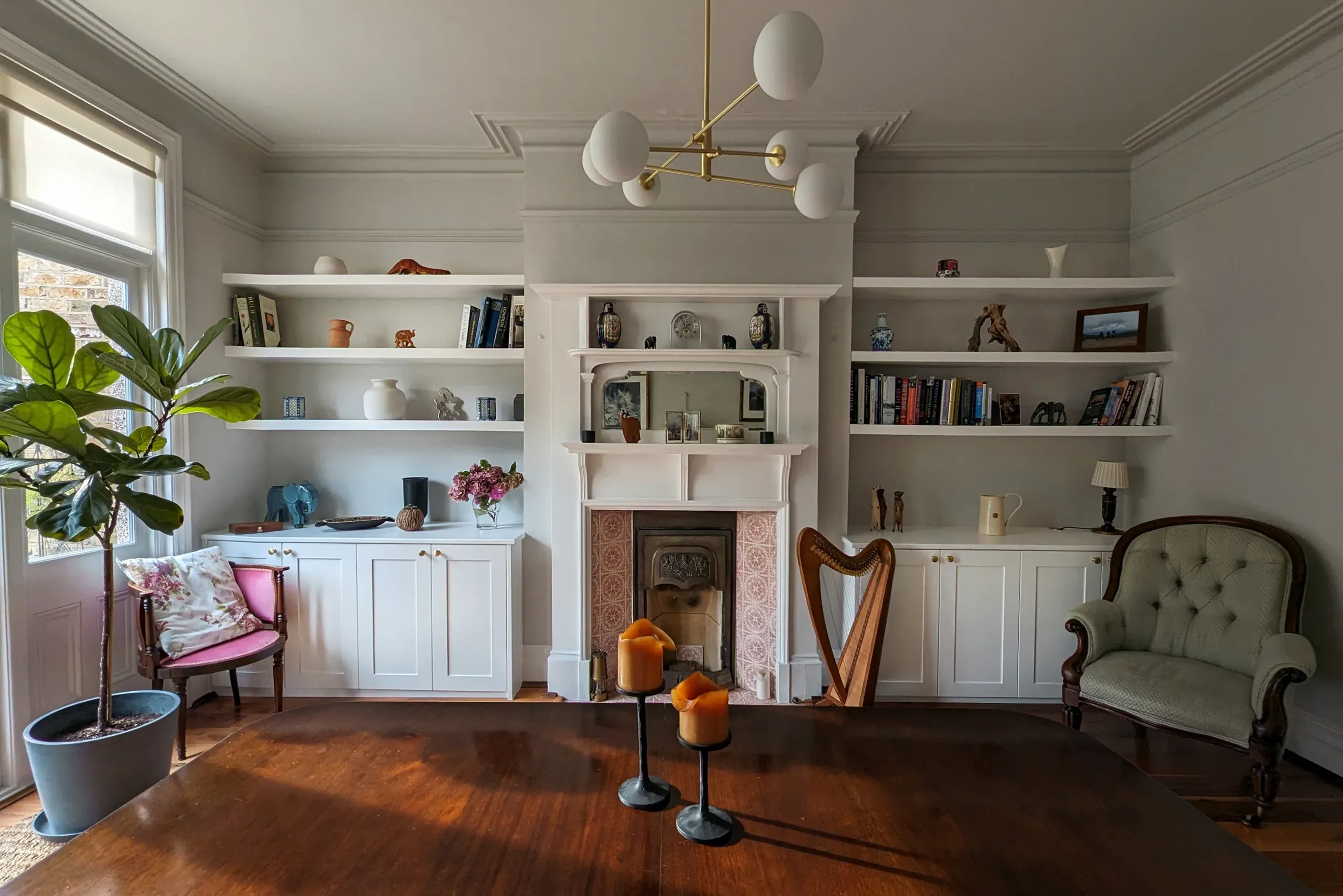 Living room with built-in bookshelves, fireplace, chairs, and a harp. Wooden floors, gray walls, and a large plant.
