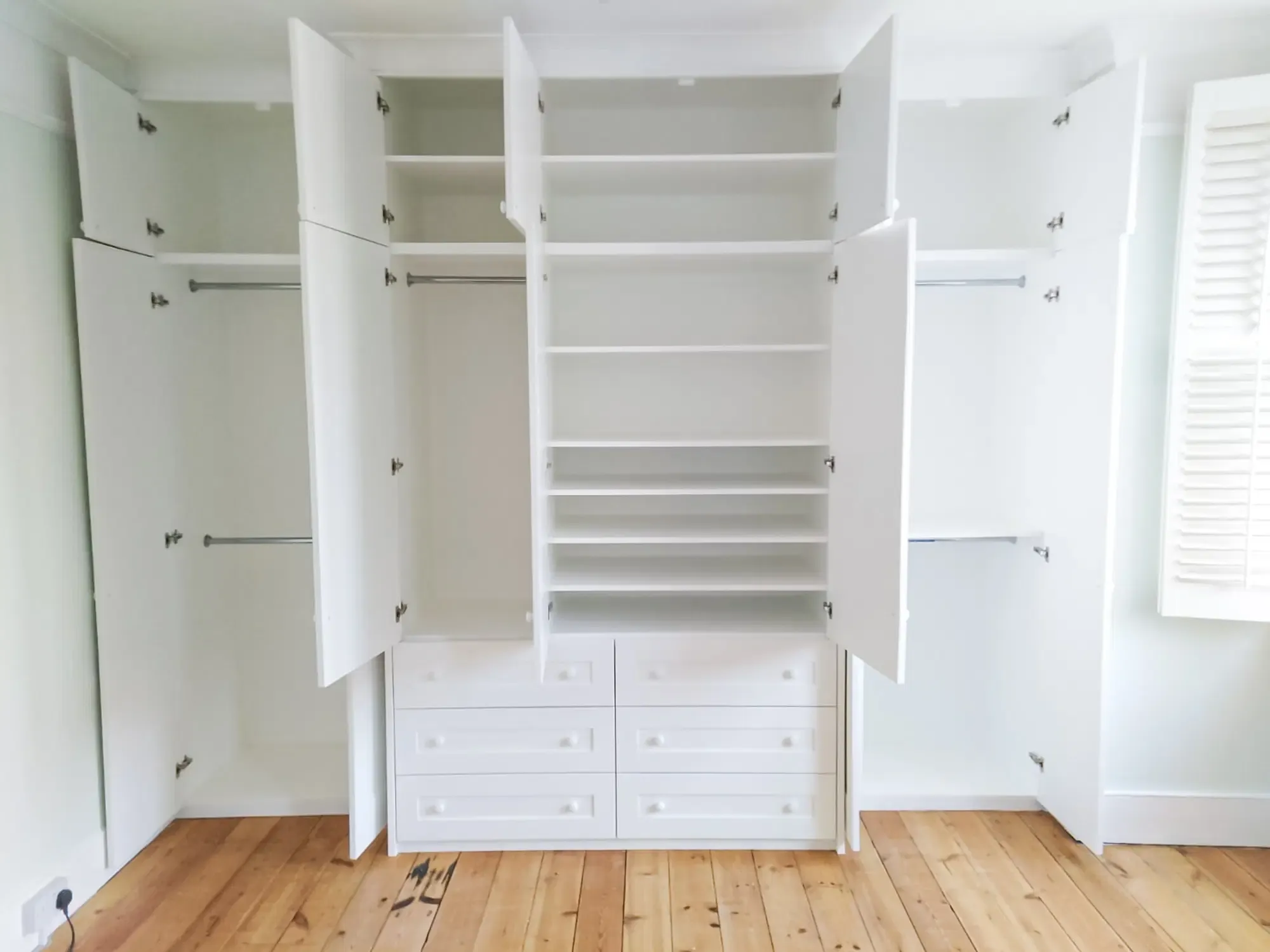 White wardrobe with open doors, wooden floors, shelves, and drawers.