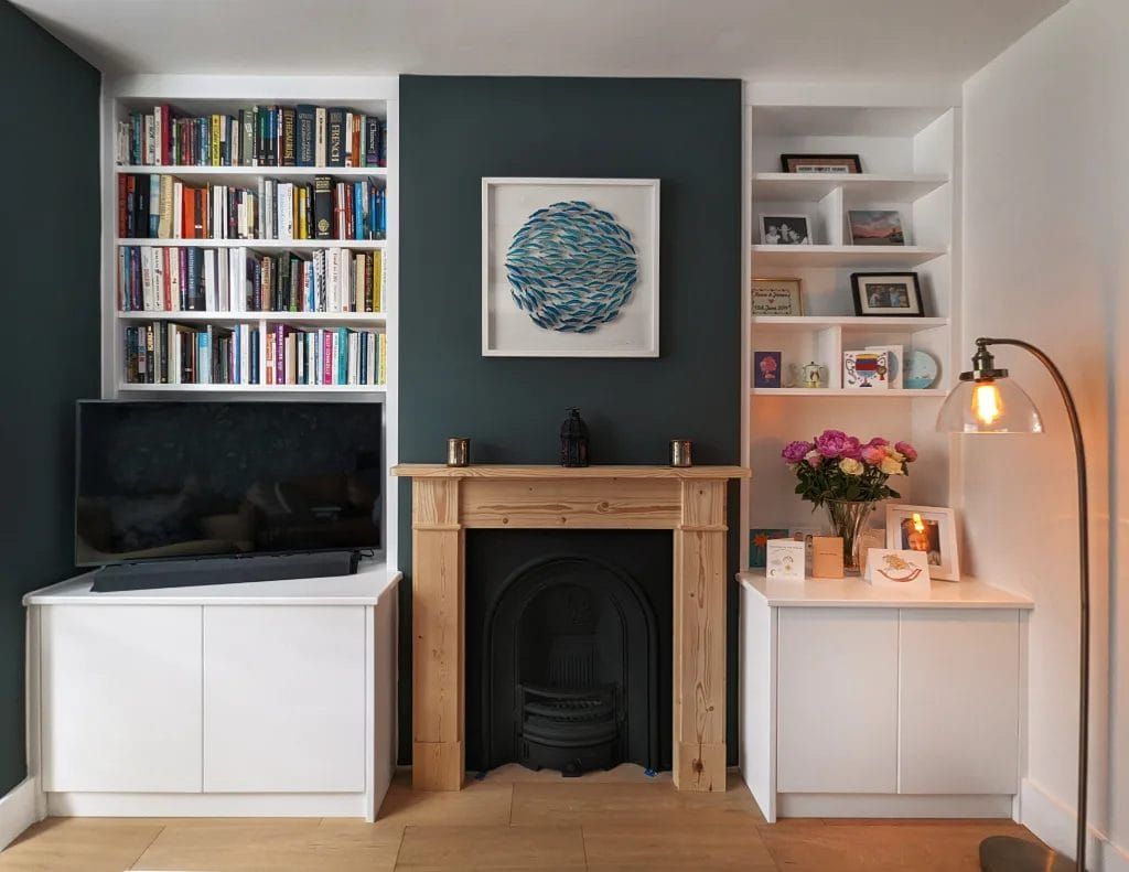 Built-in white bookshelves flank a dark teal wall with a fireplace. A TV sits below one set of shelves.