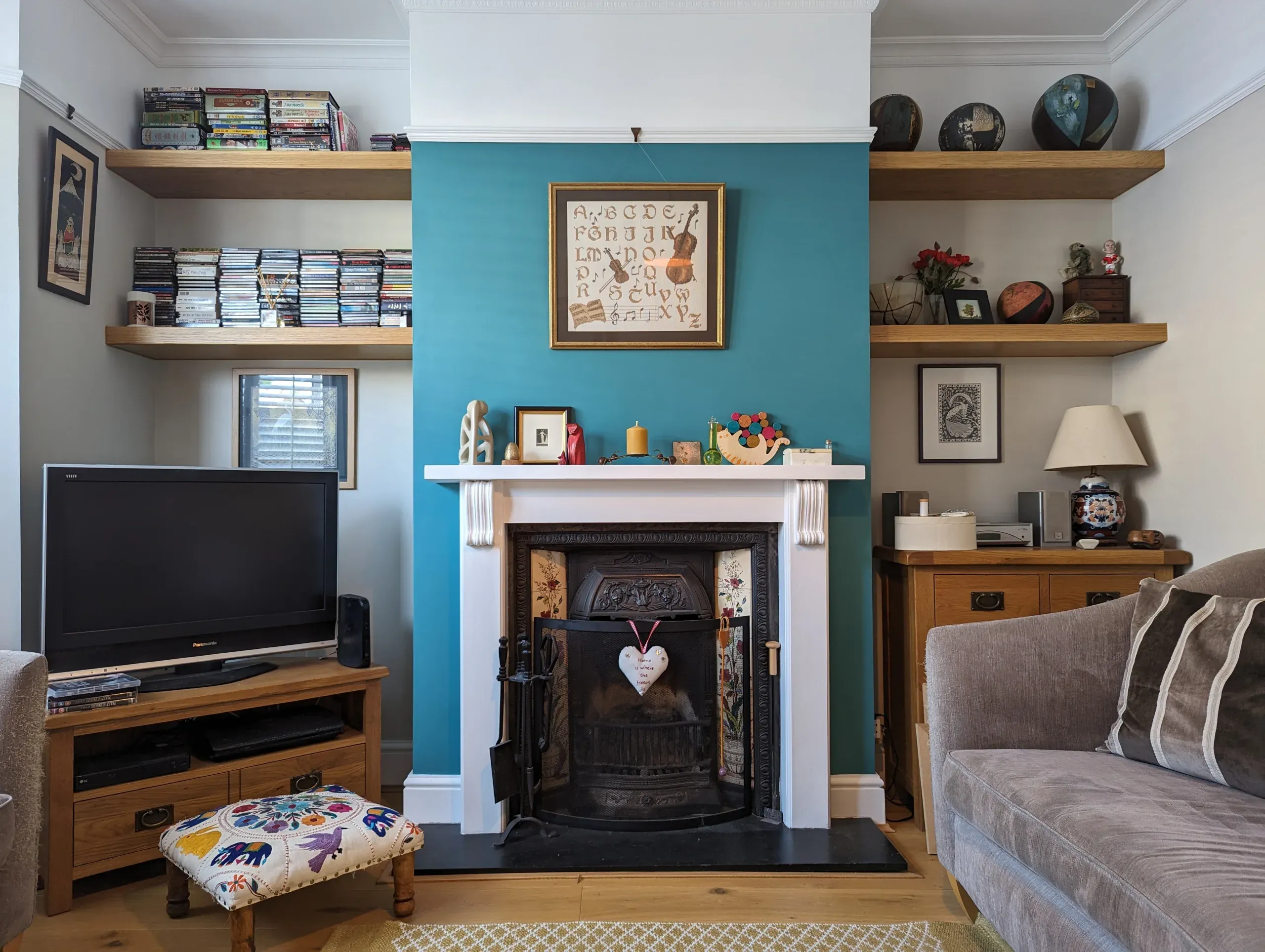 Living room with teal accent wall, fireplace, shelves, and small sofa.