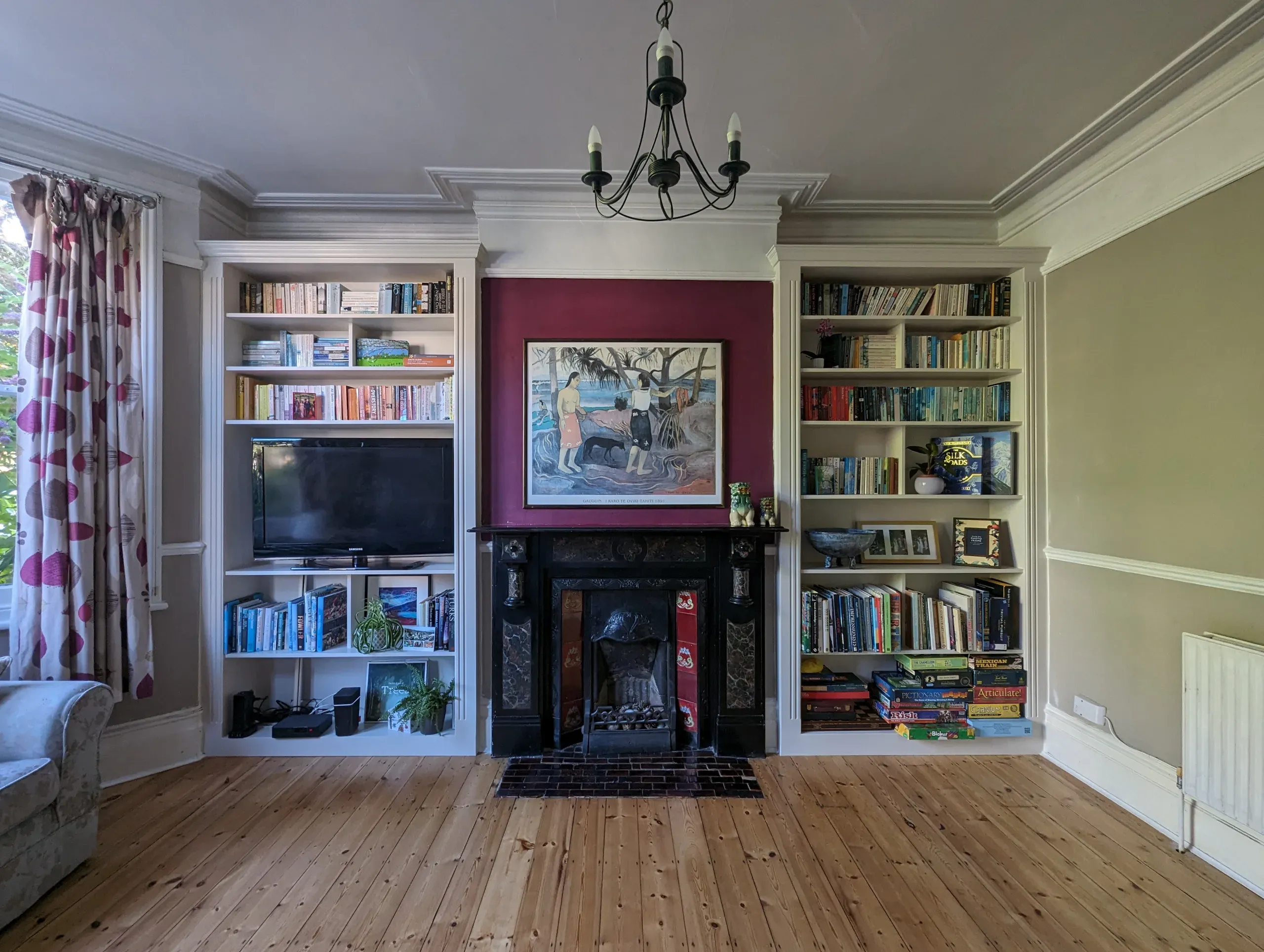 Living room with built-in bookshelves flanking a fireplace, wooden floors, and a chandelier.