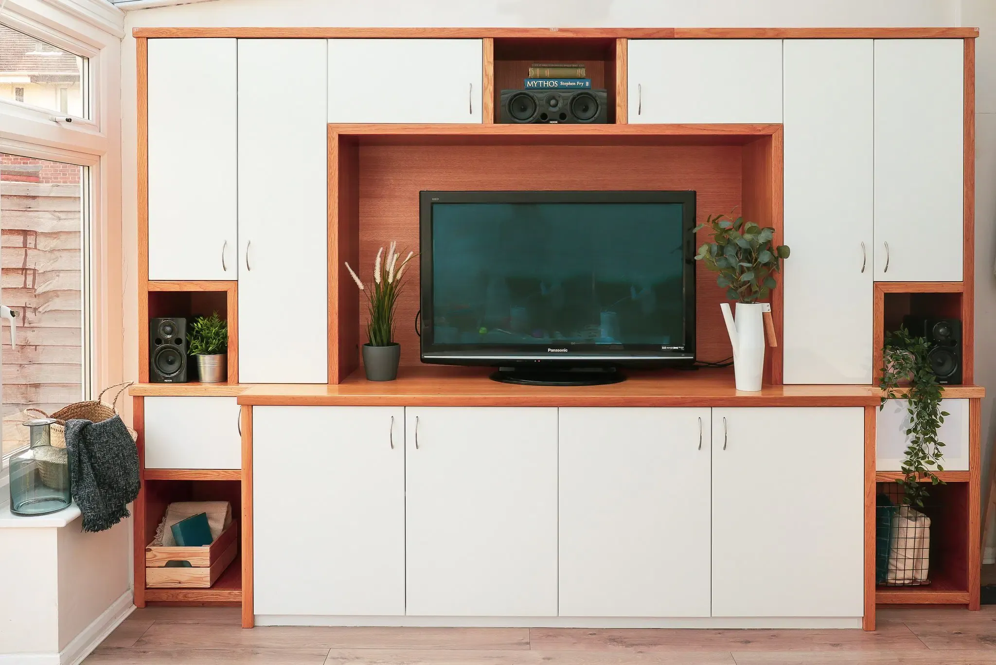 Wooden media center with white cabinets, a TV, and decorative plants.
