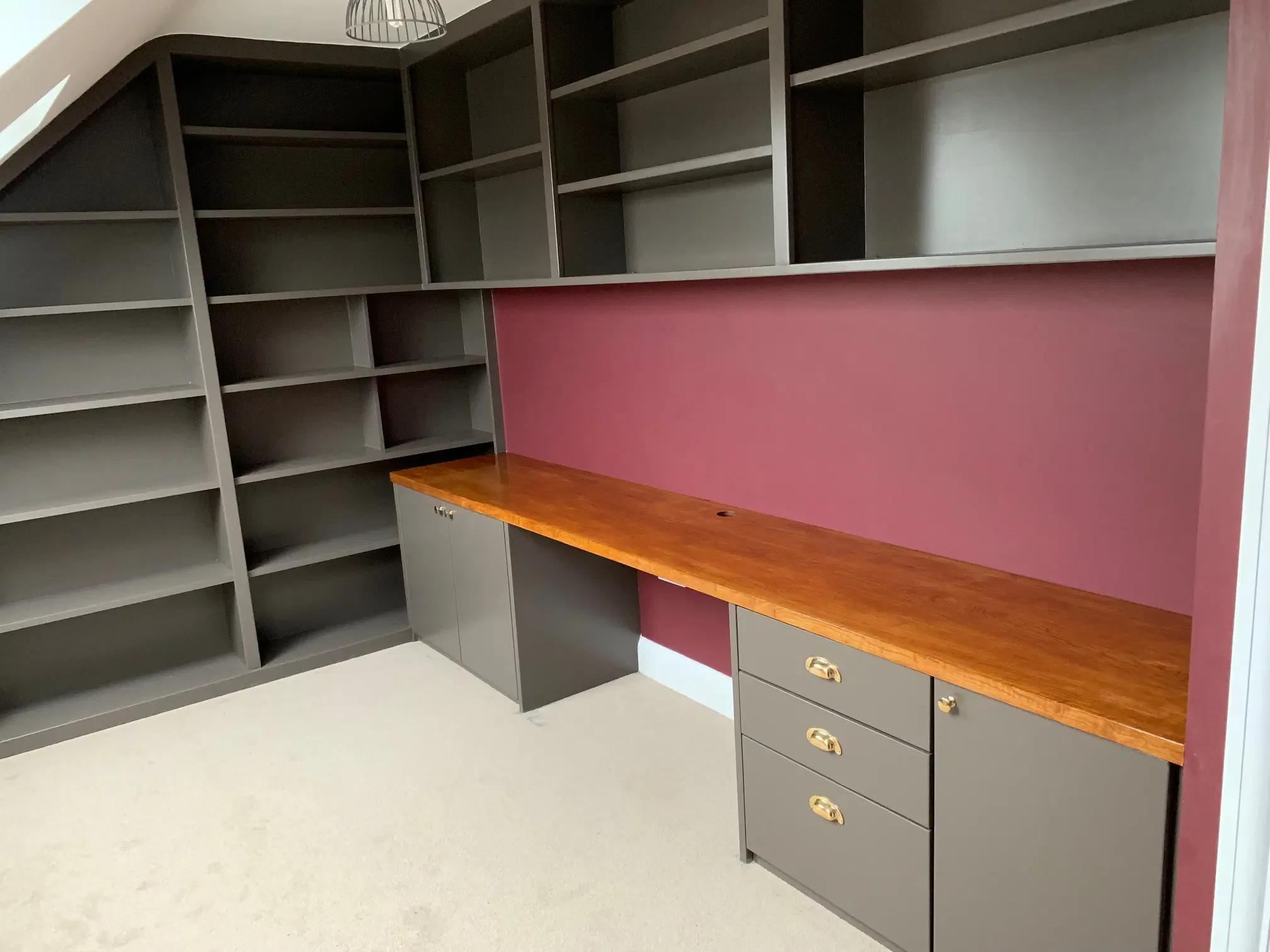 Built-in home office with dark gray shelving, a wooden desk, and burgundy accent wall.