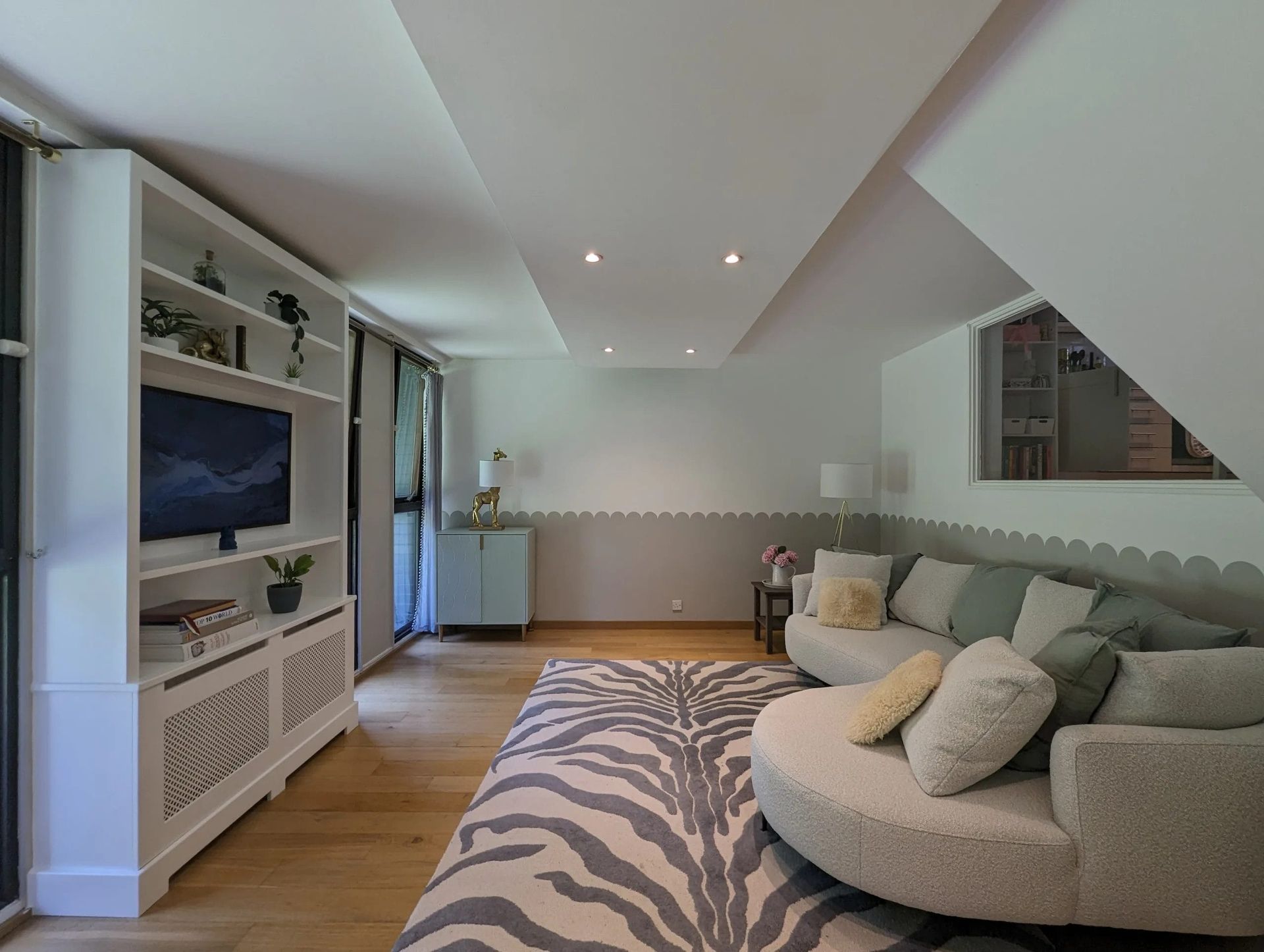 Living room with curved sofa, zebra rug, built-in shelves, TV, and wood floor.