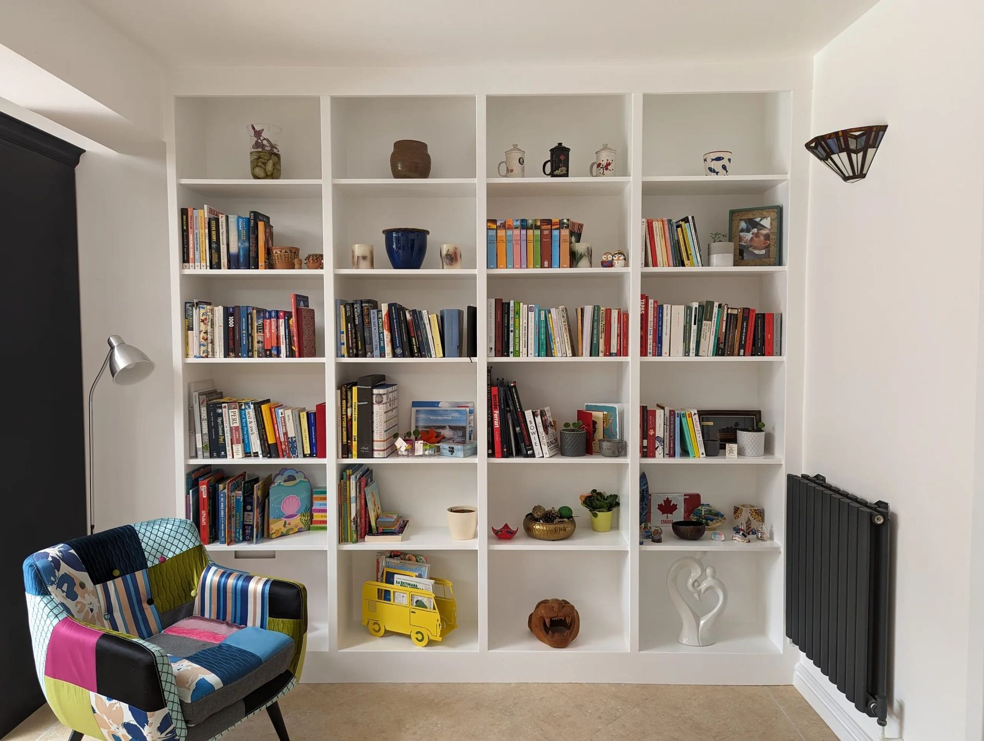 White built-in bookshelves filled with books and decorative items, a patchwork chair, and a radiator.
