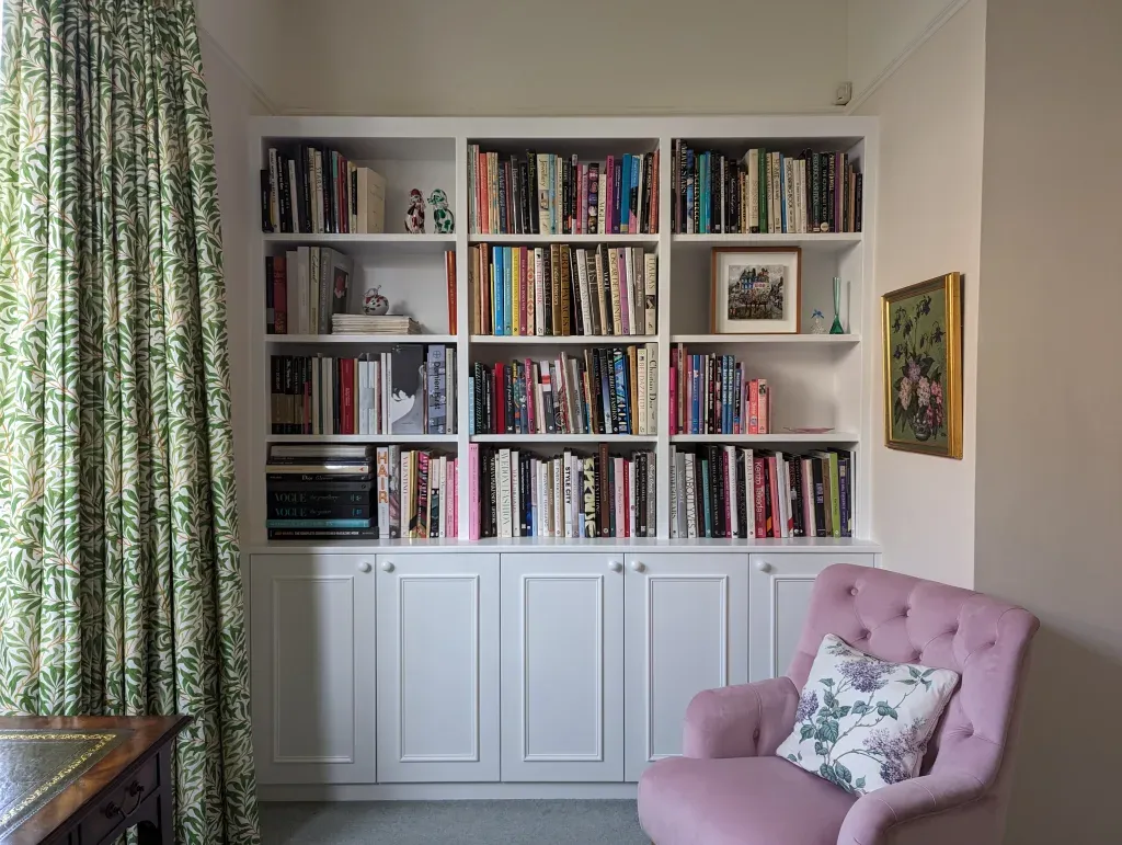 Built-in white bookshelves filled with books, a pink armchair, and green patterned curtains.