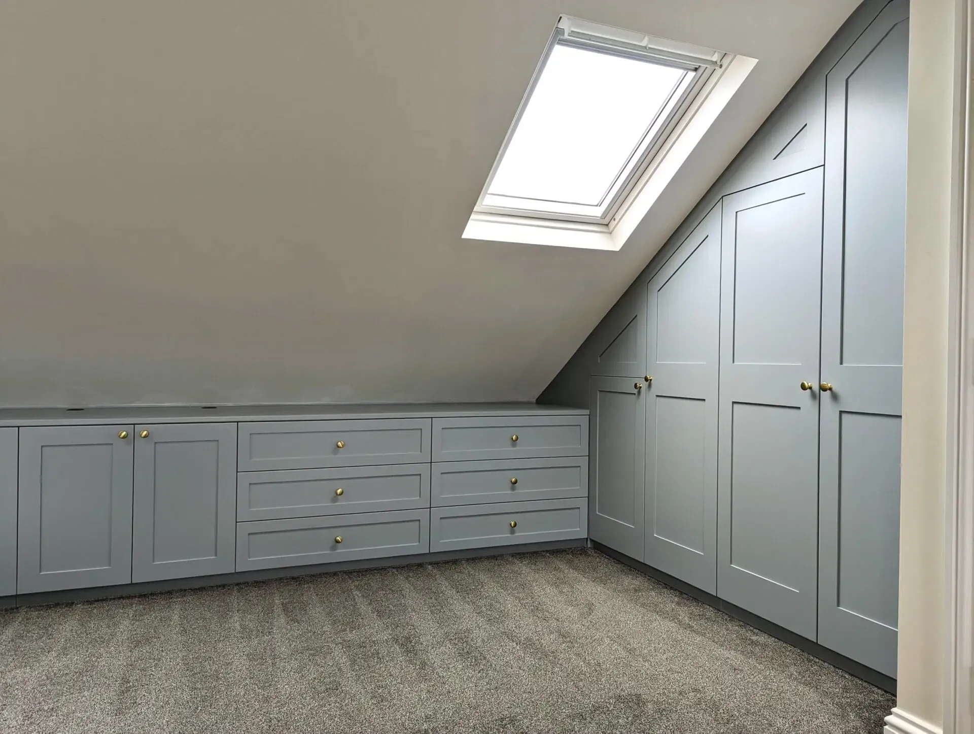 Gray built-in storage cabinets in an attic with a slanted ceiling and a skylight.