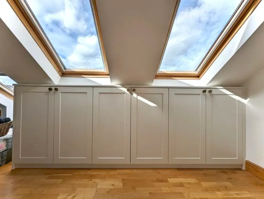 Built-in white cabinets below two skylights, wooden floor. Bright room, sunlight.