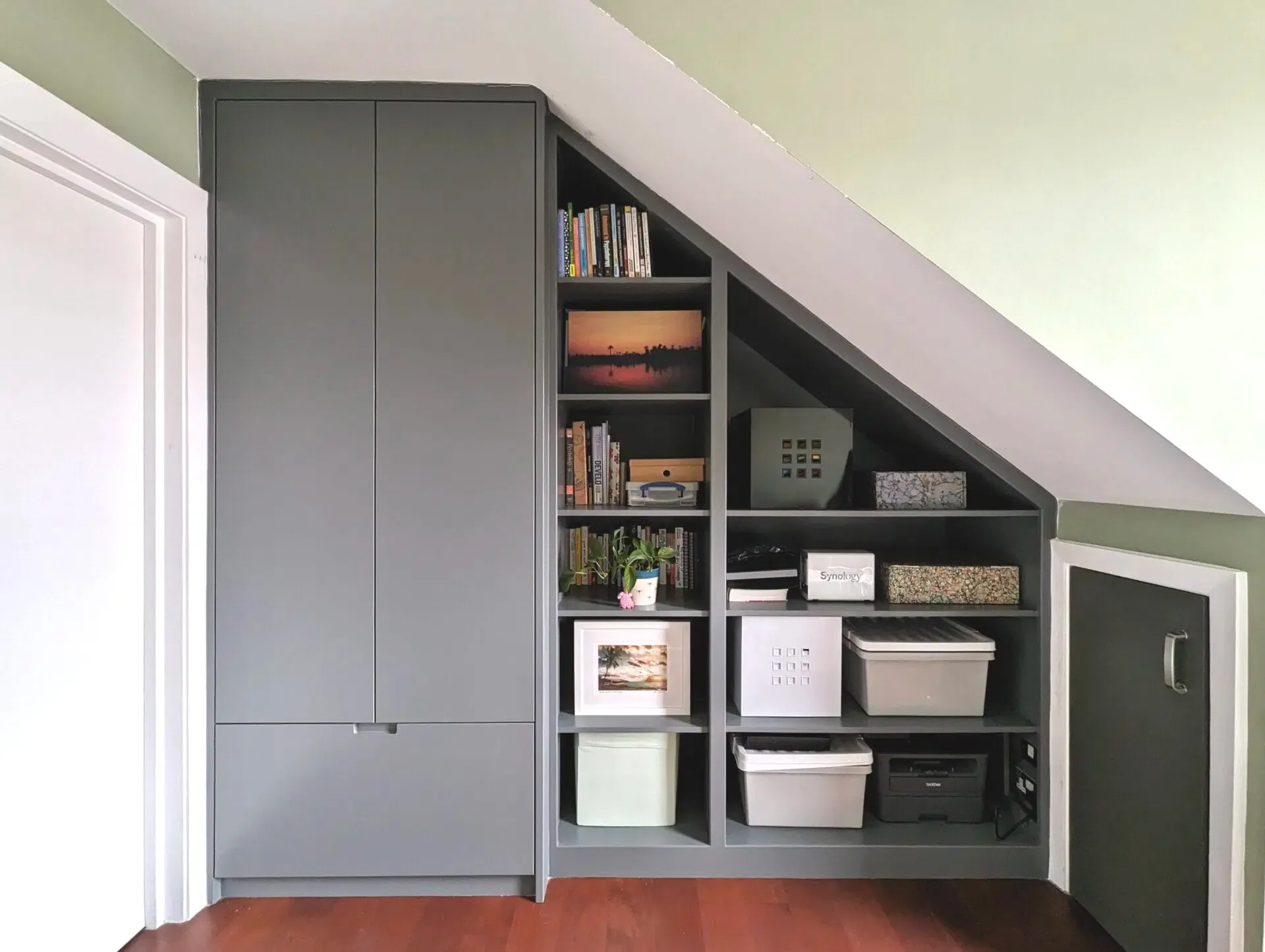 Gray built-in shelving and closet in a sloped-ceiling room, holding books and decorative items.