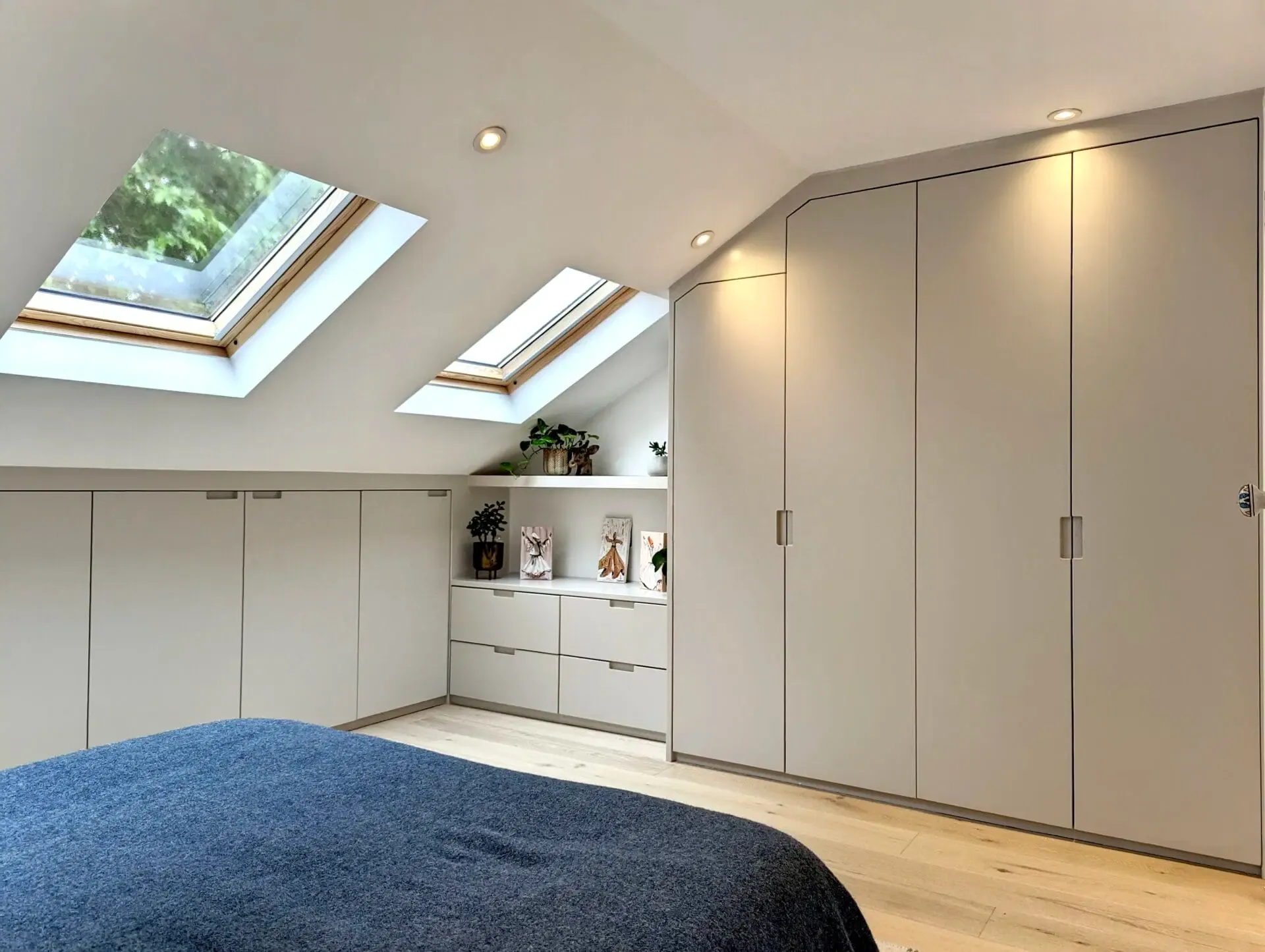 Bedroom with built-in light gray cabinets, two skylights, wooden floor, and a bed with a blue comforter.
