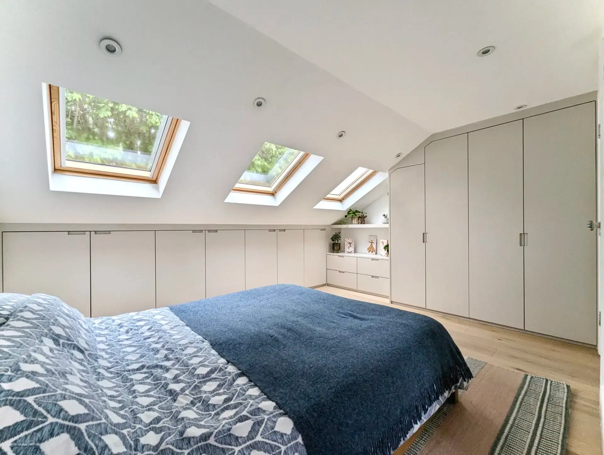 Bedroom with sloped ceiling, skylights, built-in storage, and bed with blue blanket.