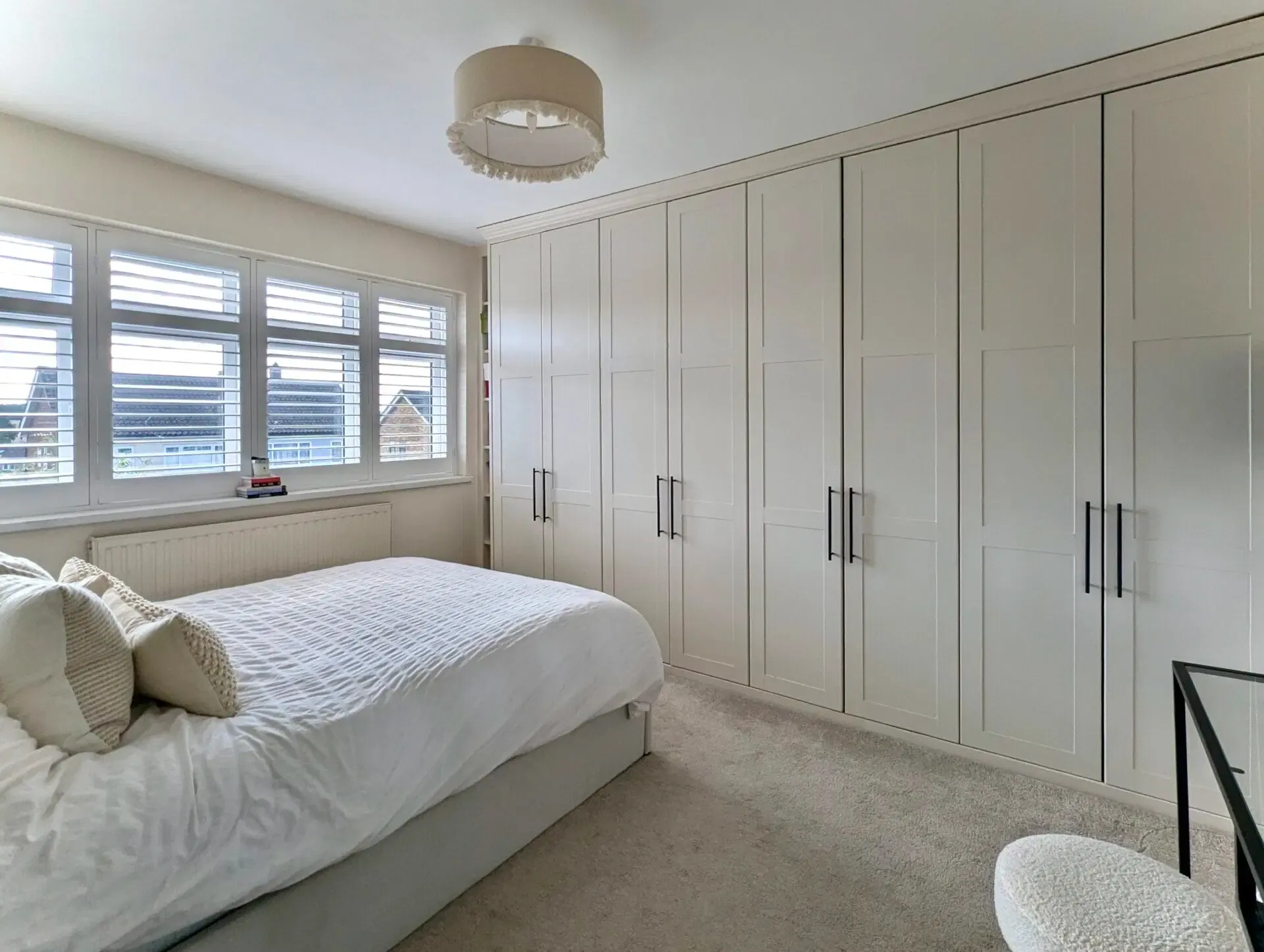 Bedroom with white built-in closets, a bed with white bedding, and a window with blinds.